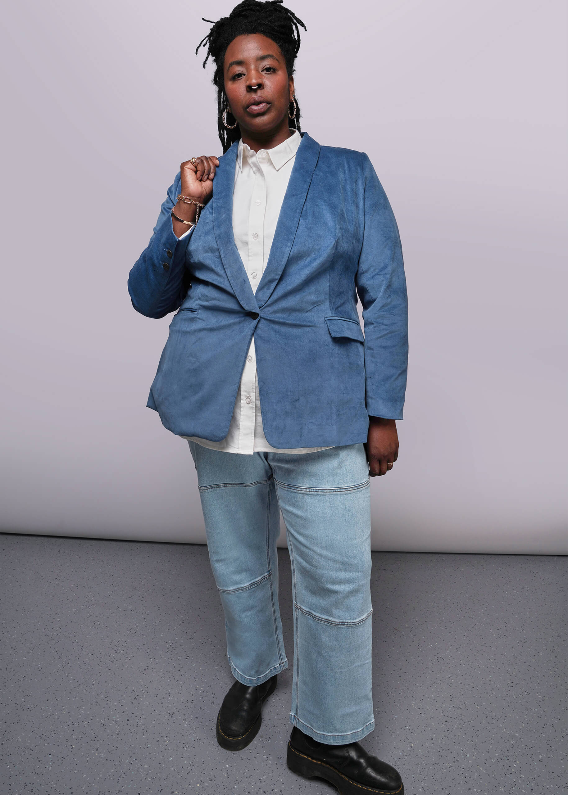 1X=Person wearing a blue blazer and jeans against a plain background