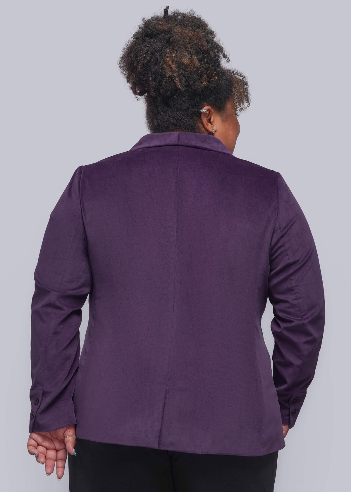 1X=A person shown from the back wearing a purple long-sleeve blazer and black pants against a light gray studio background.