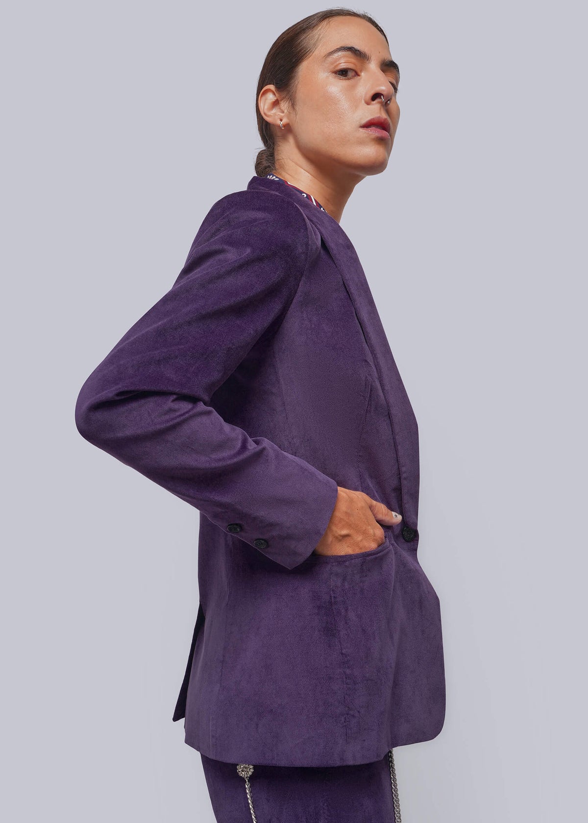 S=A model wearing a purple velvet blazer and matching trousers, shown from a side profile against a solid light gray background.