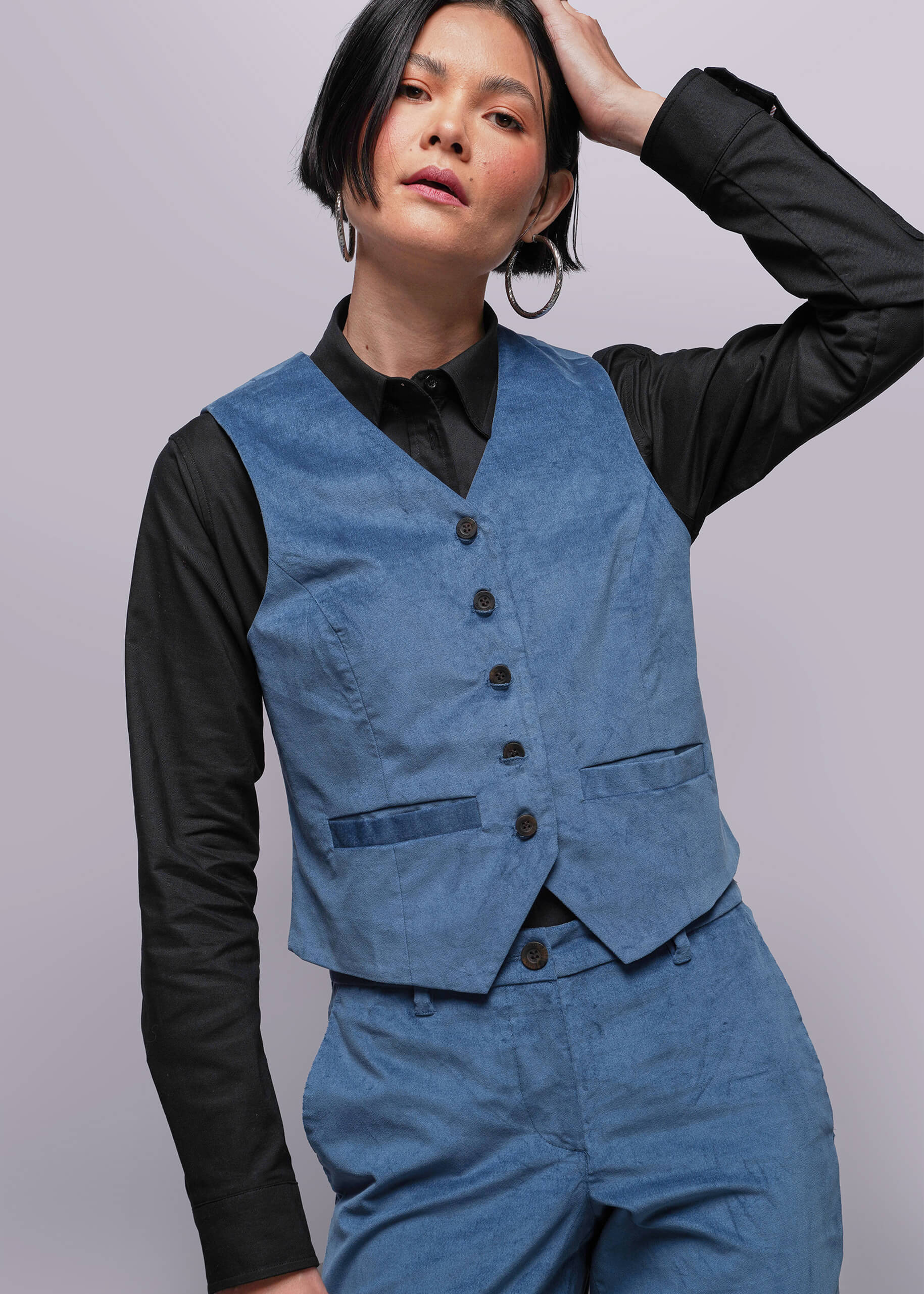 Person wearing a blue vest over a black shirt on a plain background