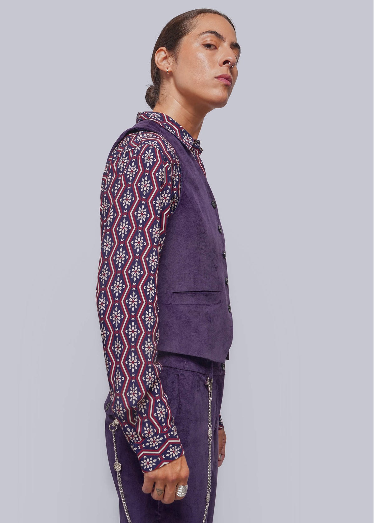 S=A model shown in profile wearing a purple vest and matching trousers, paired with a long-sleeve button-up shirt featuring a red, white, and purple geometric pattern, against a solid light gray background.