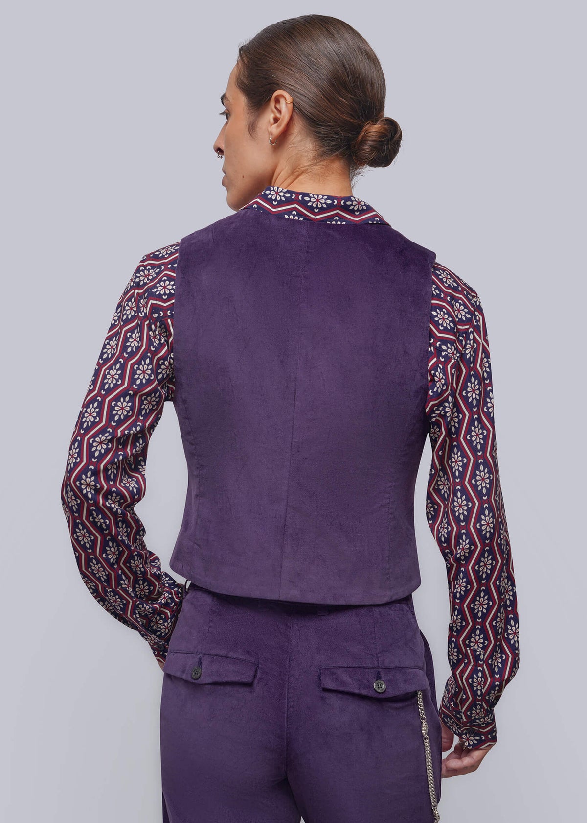 S=A model shown from the back wearing a purple vest and matching trousers, layered over a long-sleeve button-up shirt with a red, navy, and white paisley pattern, against a solid gray studio background.