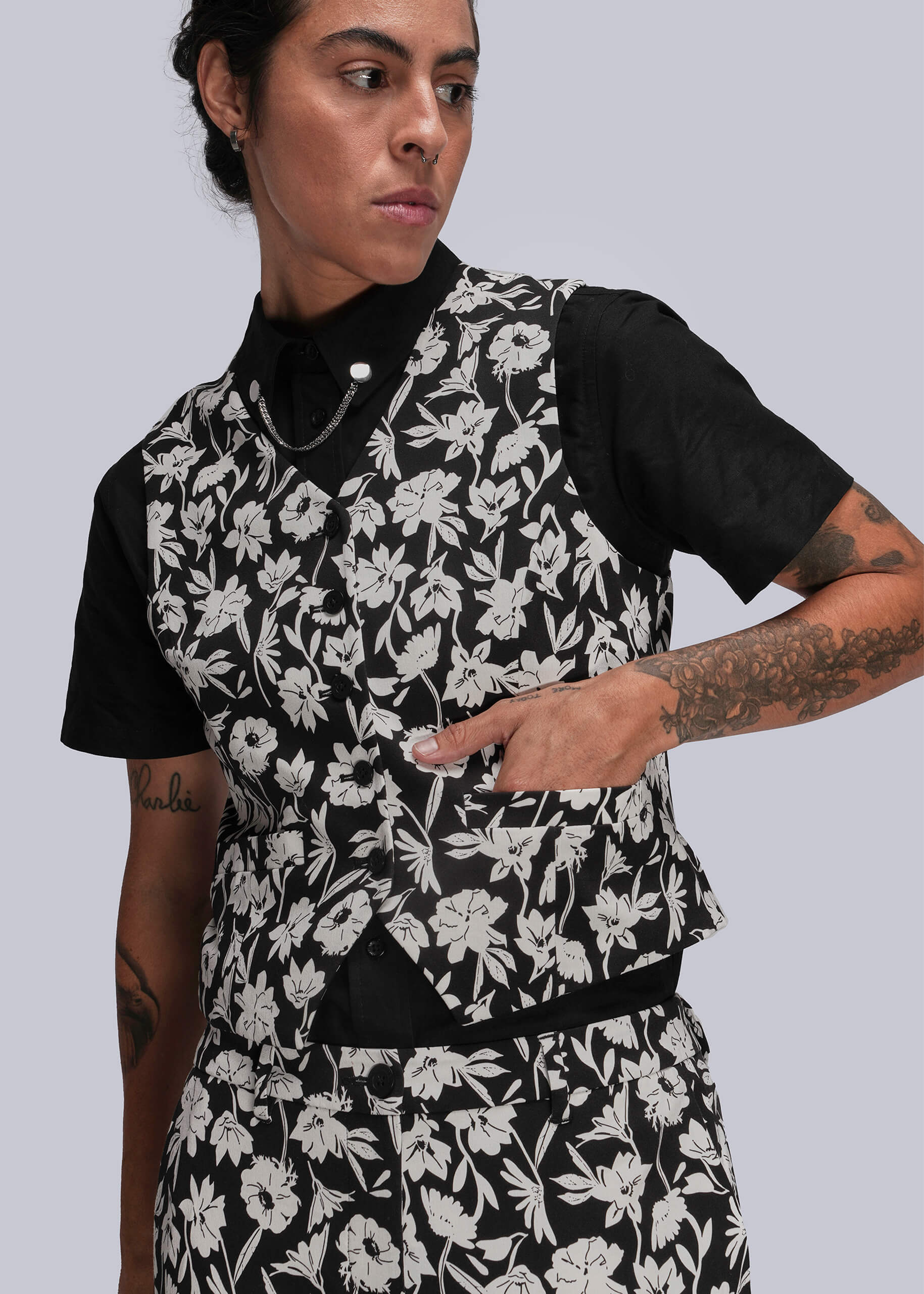 Person wearing a black and white floral vest over a black shirt on a light gray background