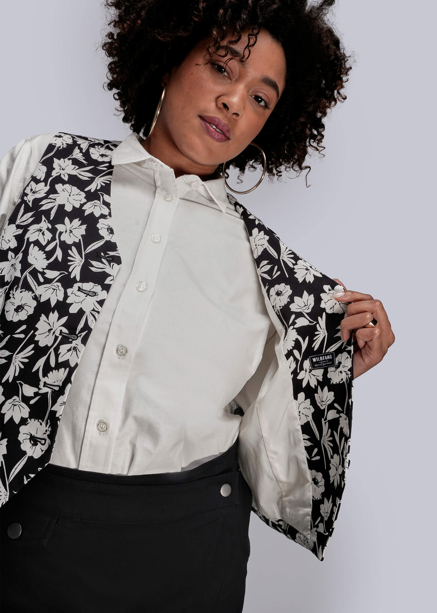 1X=Person wearing a black and white floral vest over a white shirt on a plain background