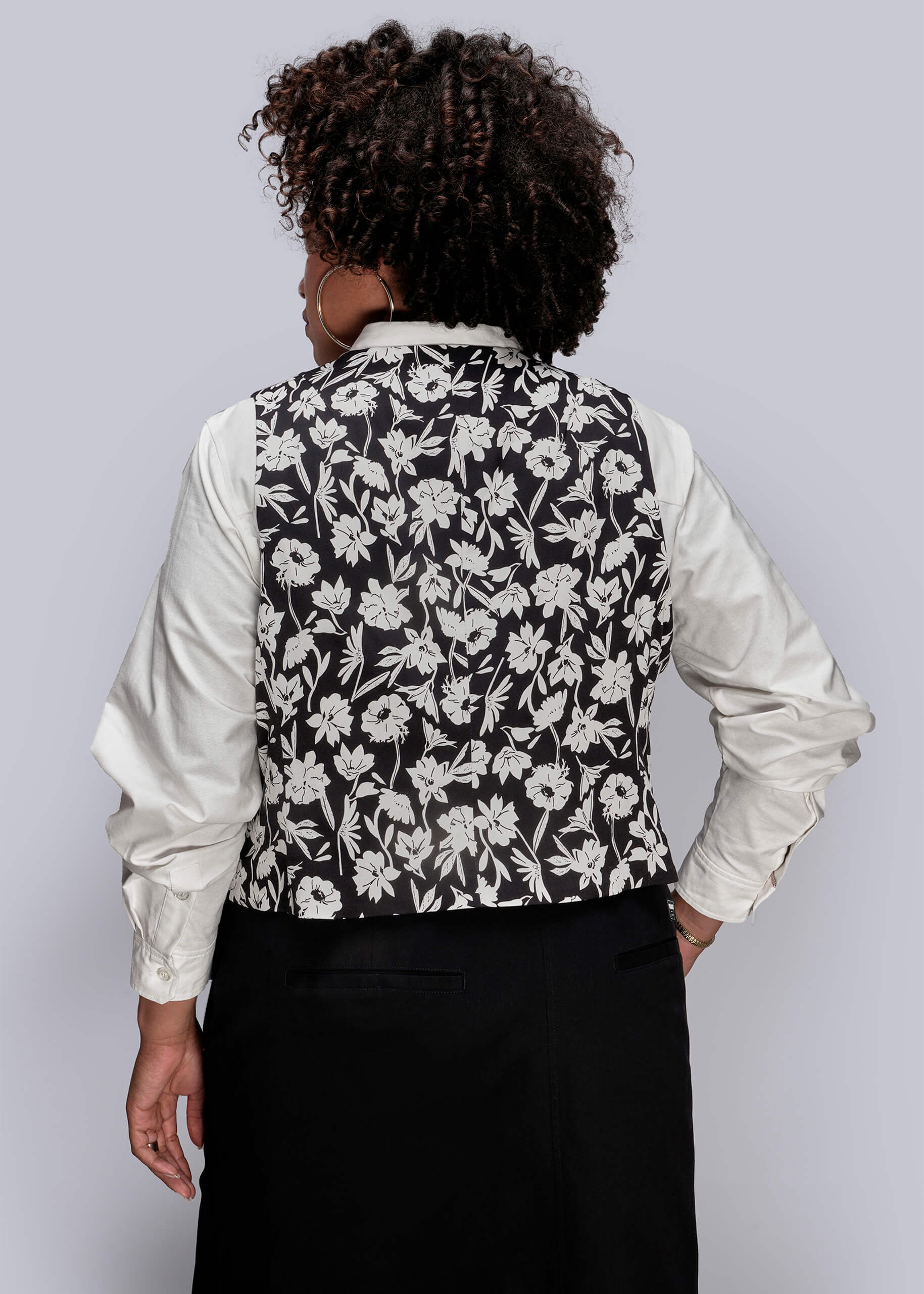 1X=Person wearing a black floral vest over a white shirt on a plain background