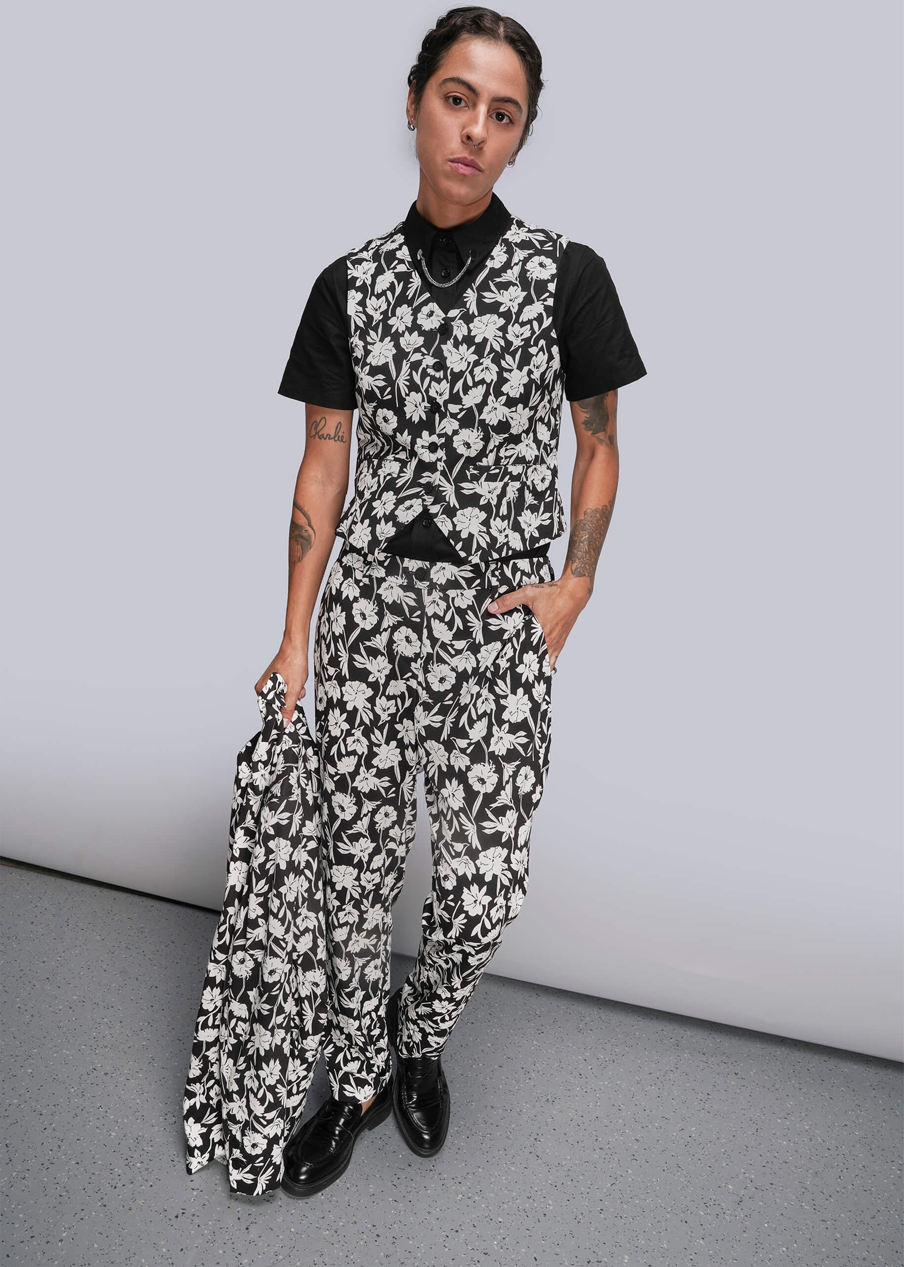 Person wearing a black and white floral suit against a gray background