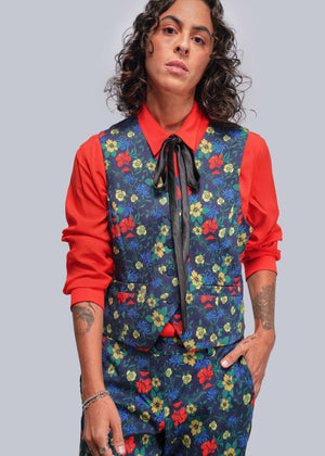 S=Person wearing a colorful floral vest over a red shirt with a plain background