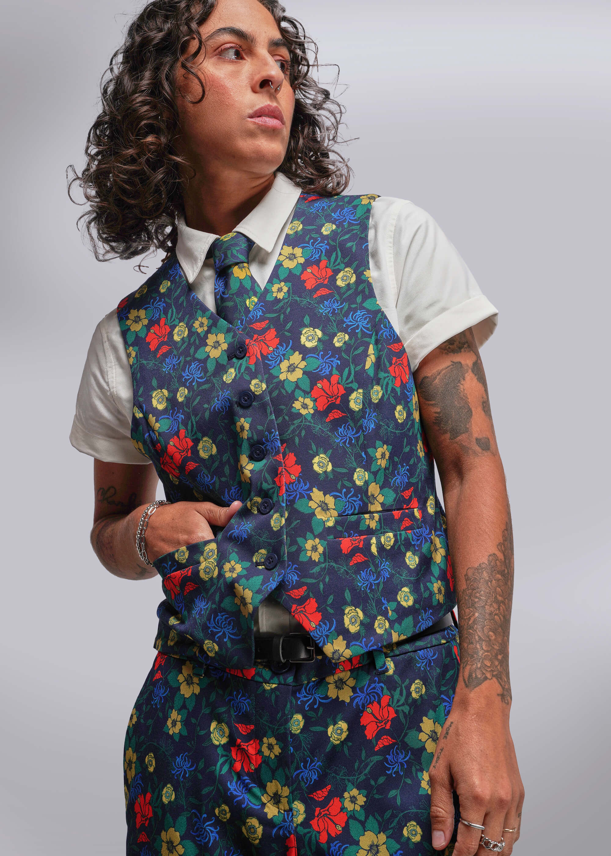 Person wearing a colorful floral vest over a white shirt on a gray background