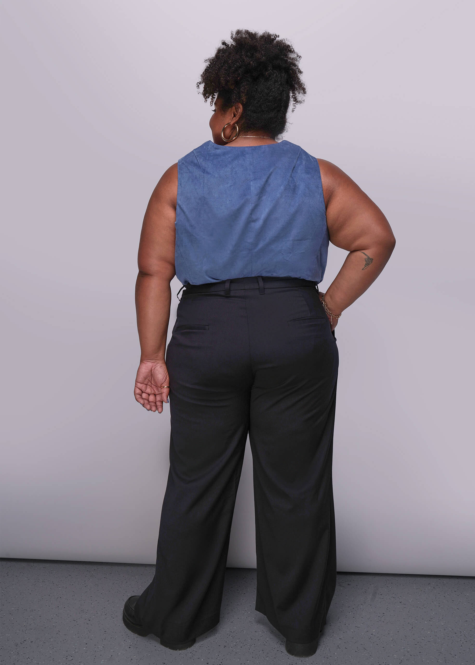 1X=Person wearing a blue sleeveless top and black pants against a plain background