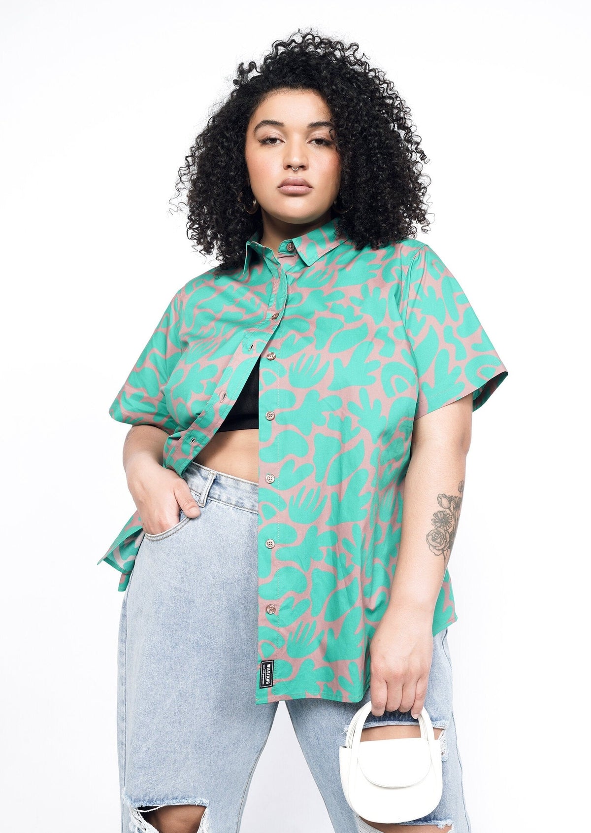 Model wearing the Essential Button Up in Abstract Emerald in size 1X with distressed jeans and a small white handbag