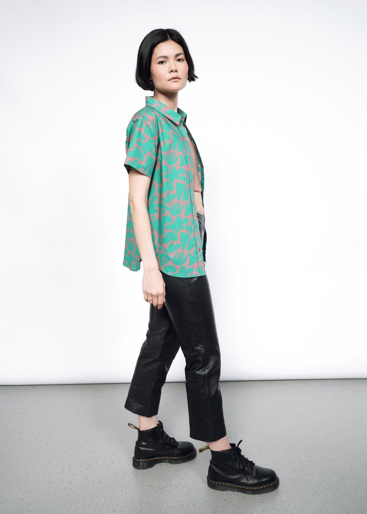 Side image of model wearing the Essential Button Up in Abstract Emerald in size XS, with black faux leather leggings and the 6-Way Corset in Rose Brown