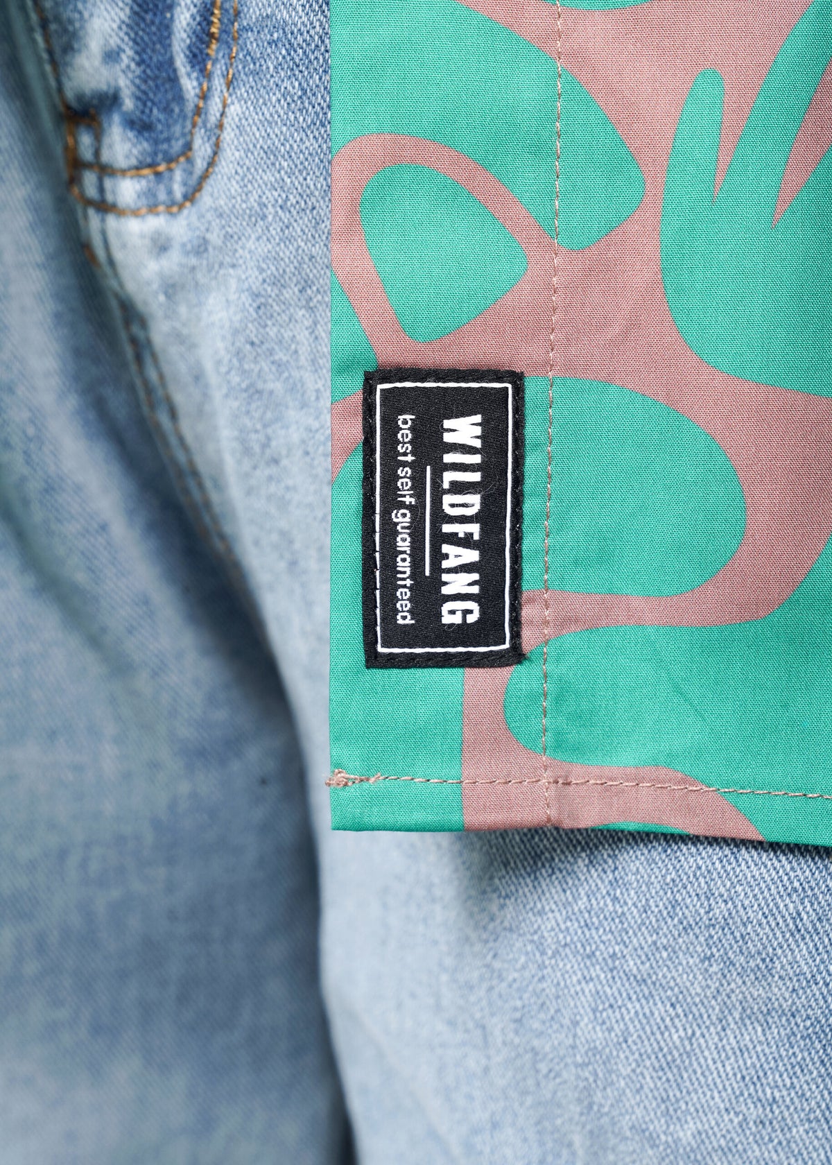 Close-up shot of the Essential Button Up in Abstract Emerald, with Wildfang - best self guaranteed - label