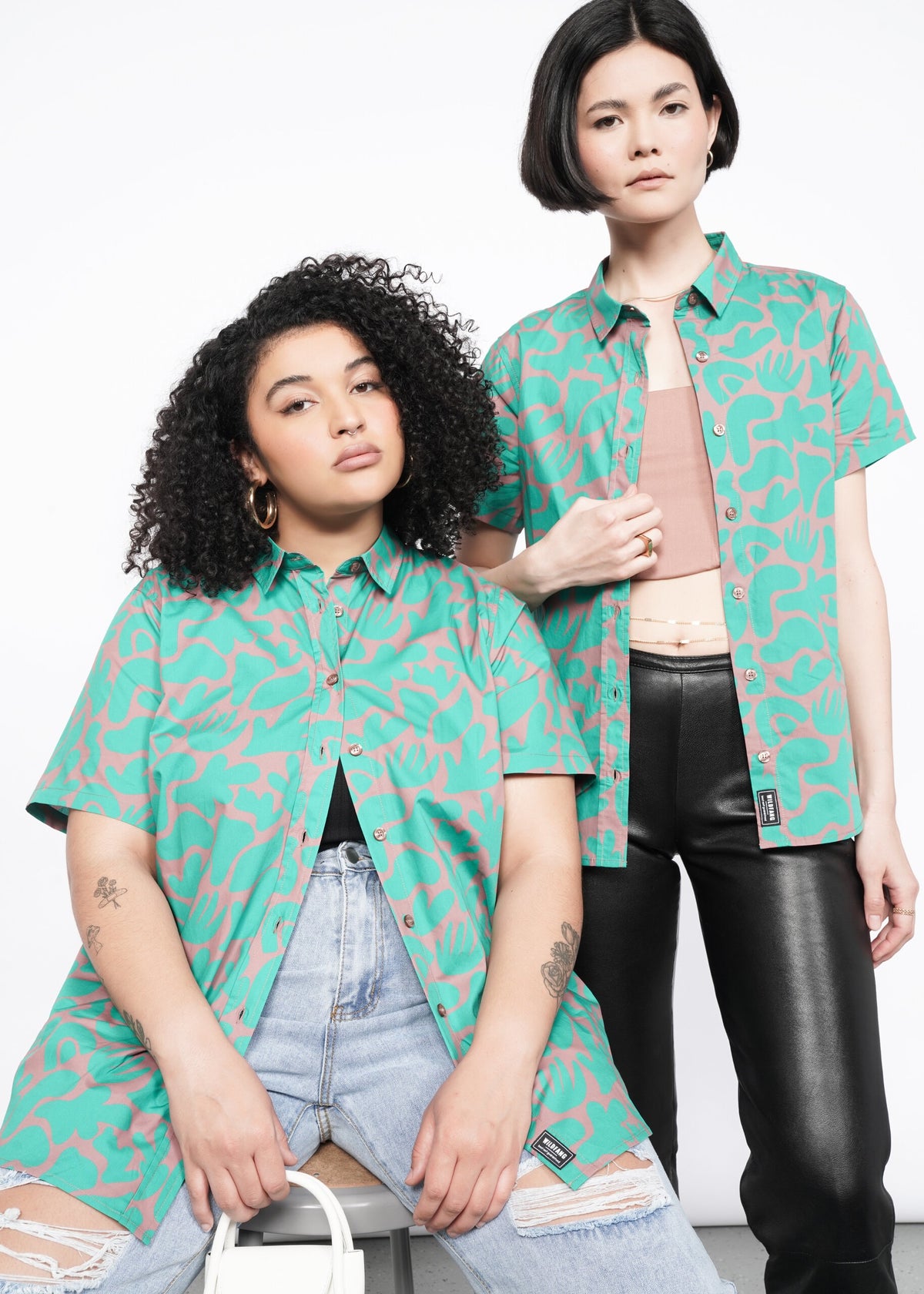 2 models wearing the Essential Button Up in Abstract Emerald. One sitting wearing distressed jeans, one standing wearing faux leather leggings