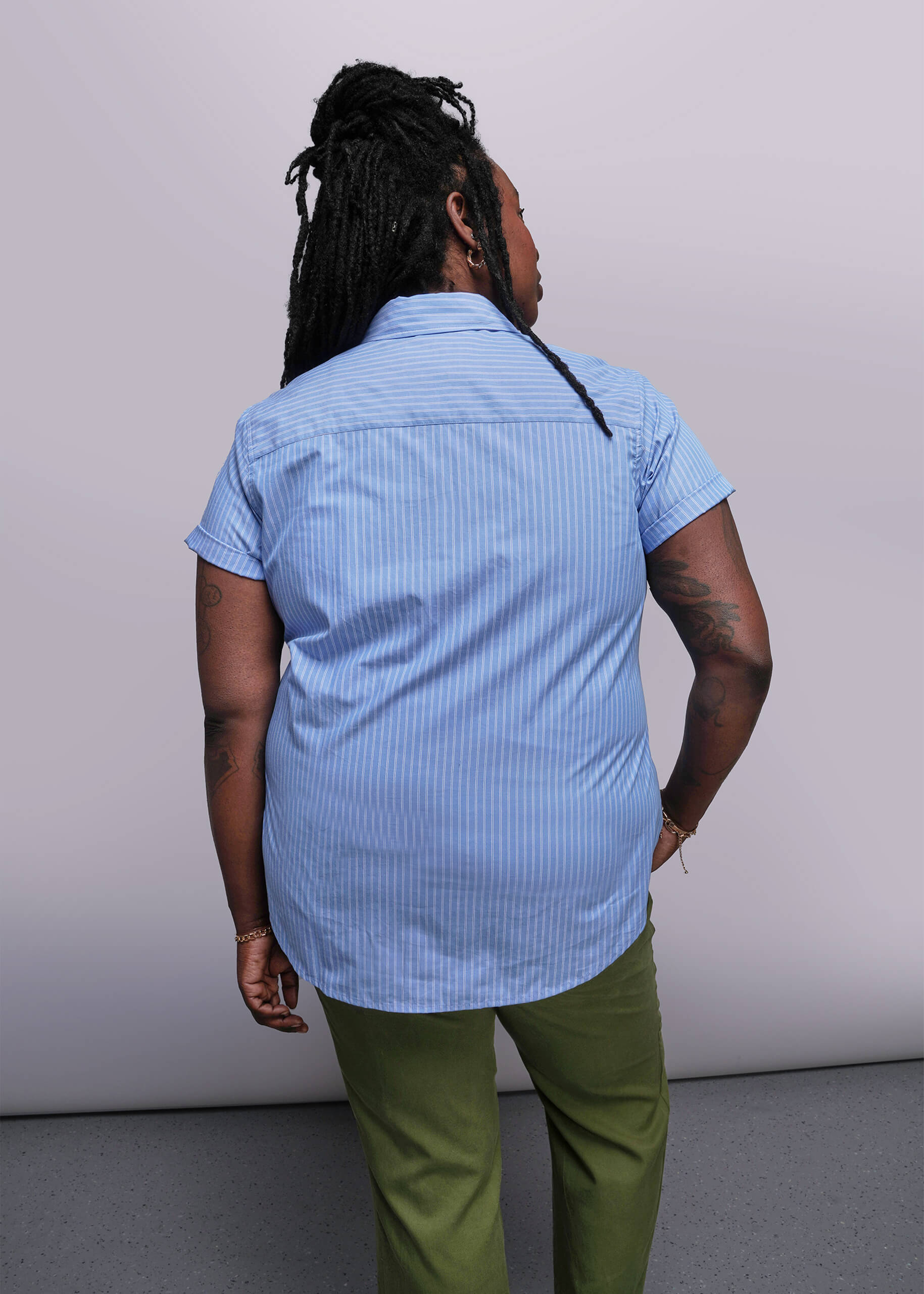 1X=Back view of person wearing a blue striped shirt and green pants against a plain background