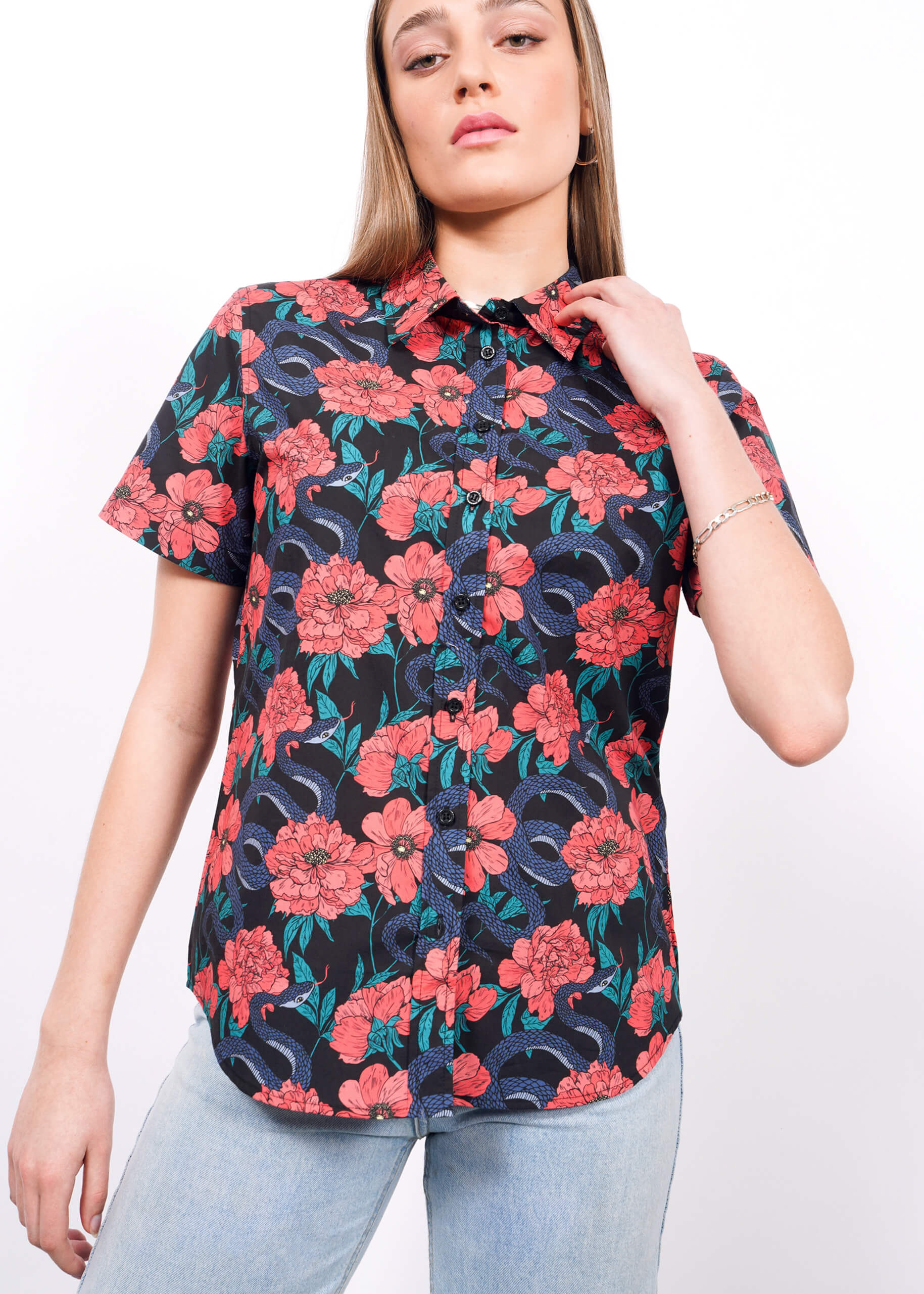A woman wears The Essential Button Up by Wildfang, featuring a bold red, blue, and green floral pattern on breathable cotton, paired with light blue jeans as she poses against a plain white background.