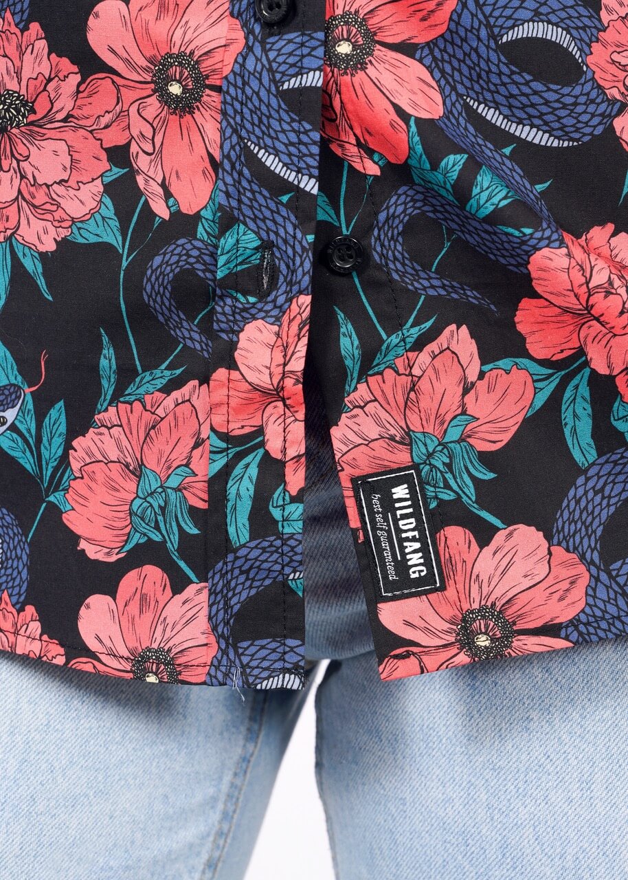 A close-up of The Essential Button Up by Wildfang, featuring pink flowers and blue snakes on black cotton. Partially unbuttoned and styled with light blue jeans, its tailored fit offers stylish comfort. Label reads WILDFANG.