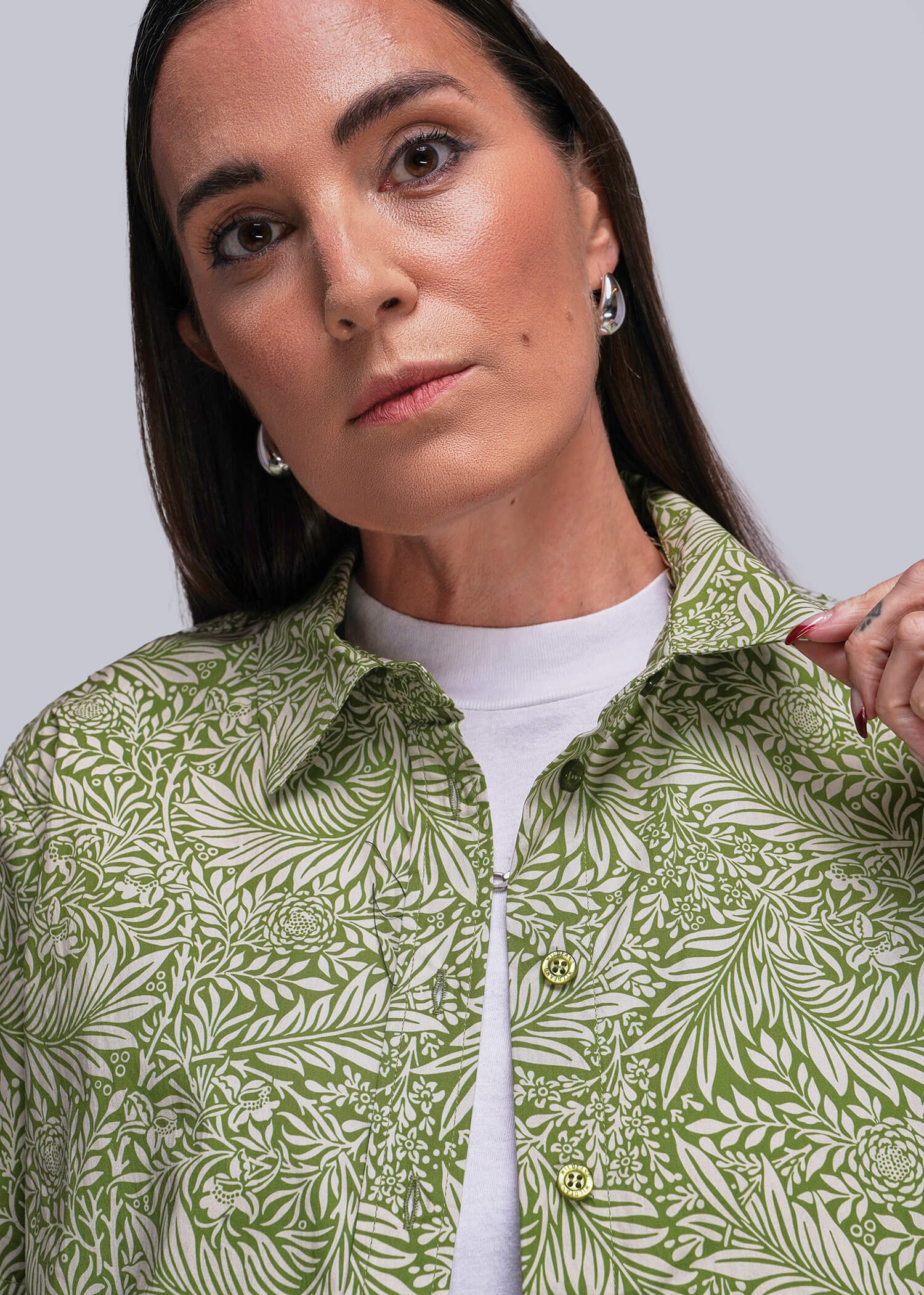 Woman wearing a green patterned shirt over a white top against a gray background