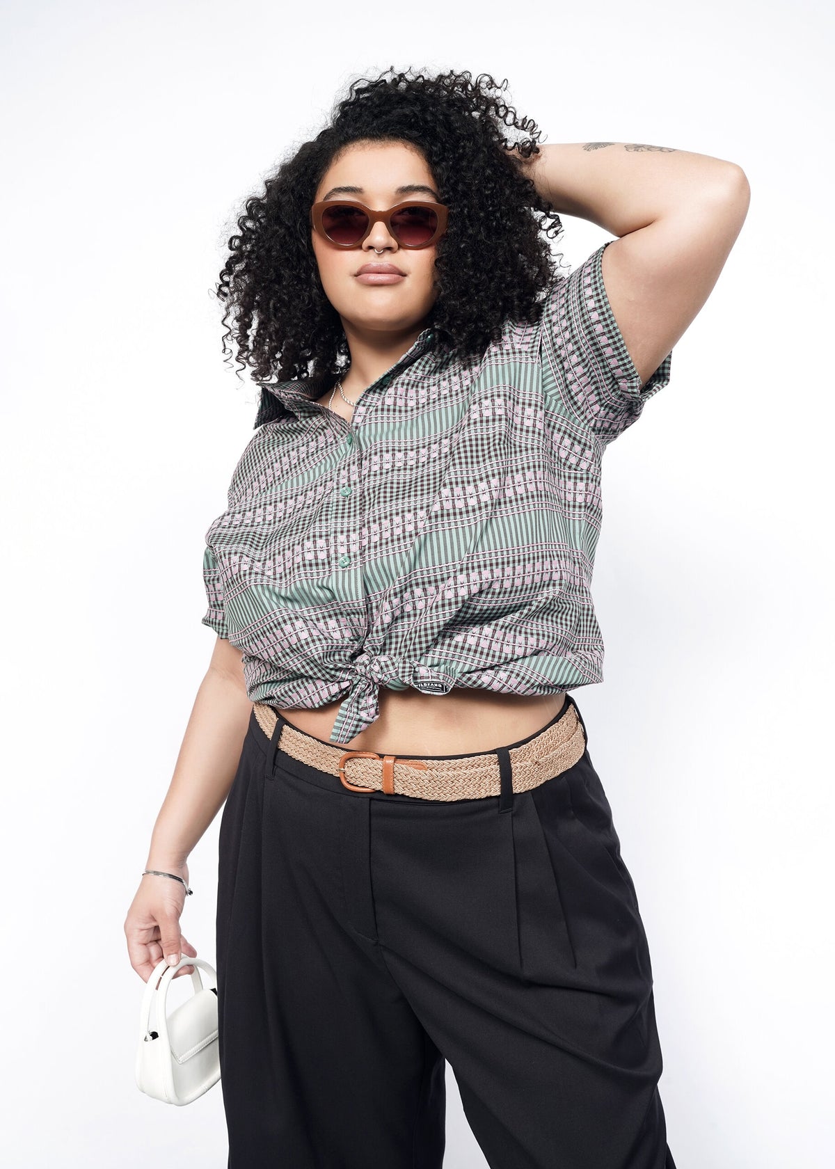 Model wearing the Essential Button Up in Gingham Sage in size 1X, tied in a low knot with black pants and a tan belt