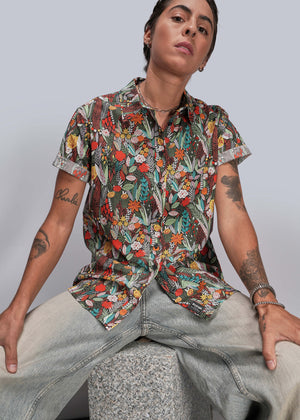 S=Person wearing a colorful floral shirt and light jeans against a plain background