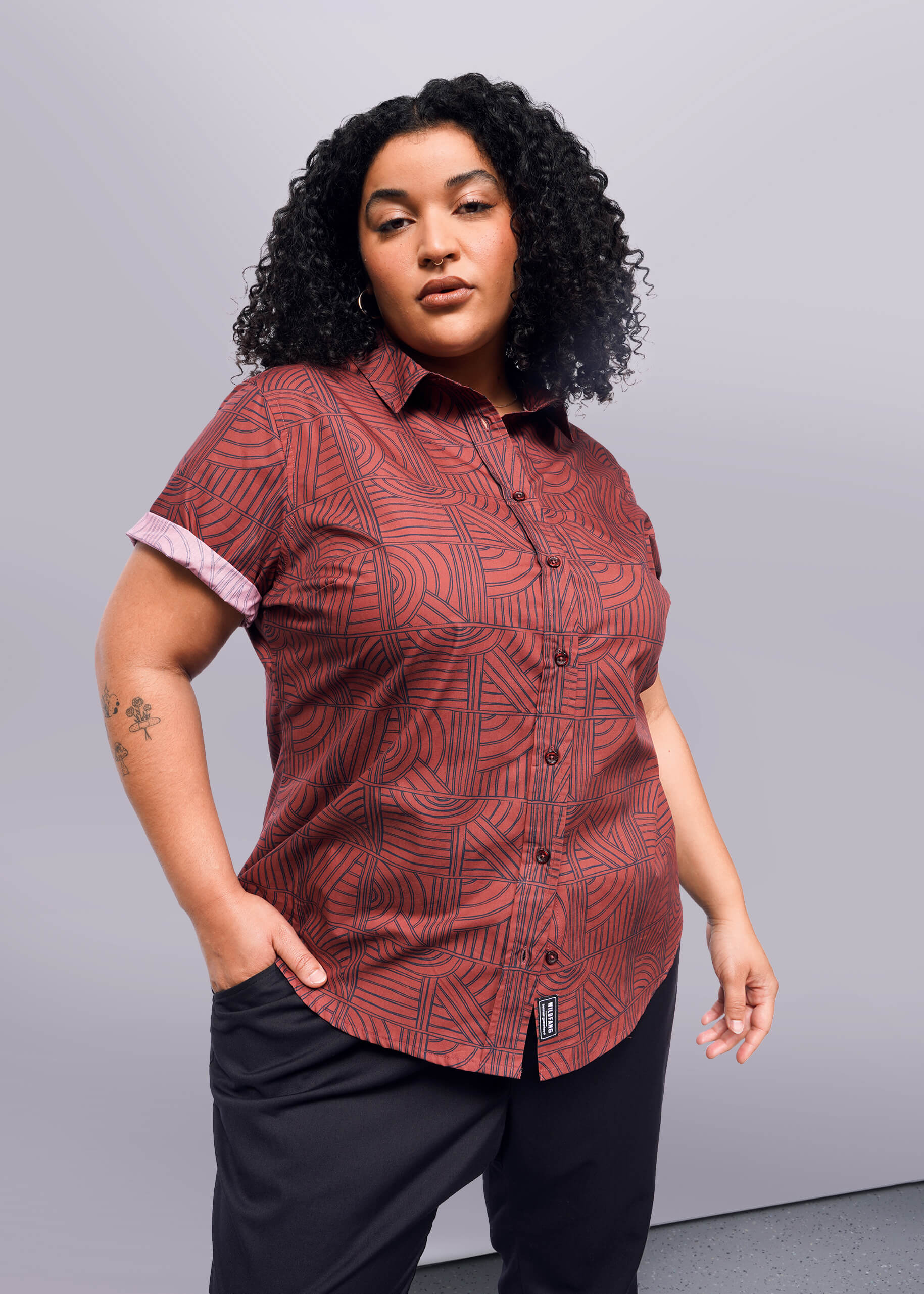 1X=A person wearing a short-sleeved button-up shirt with a geometric pattern in shades of brown and red.