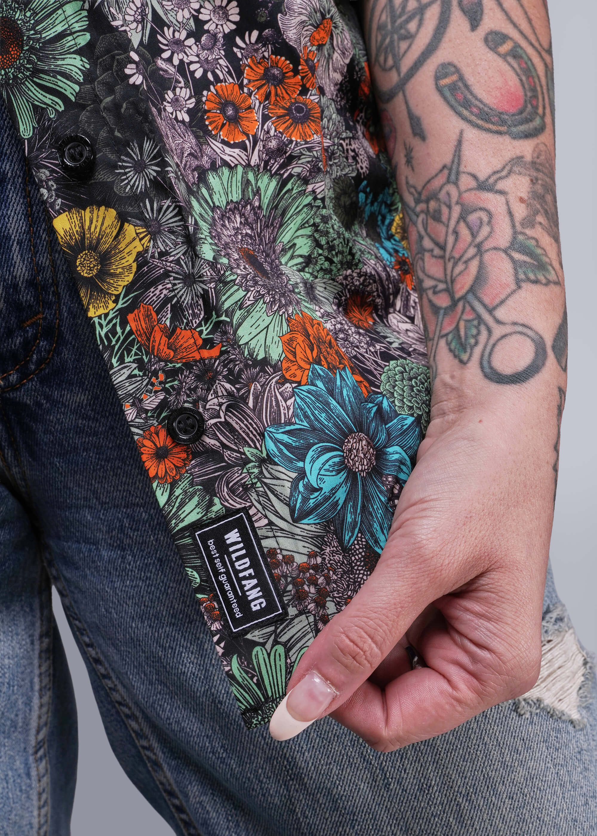 Floral patterned button up with a visible brand label, held by a person with tattoos