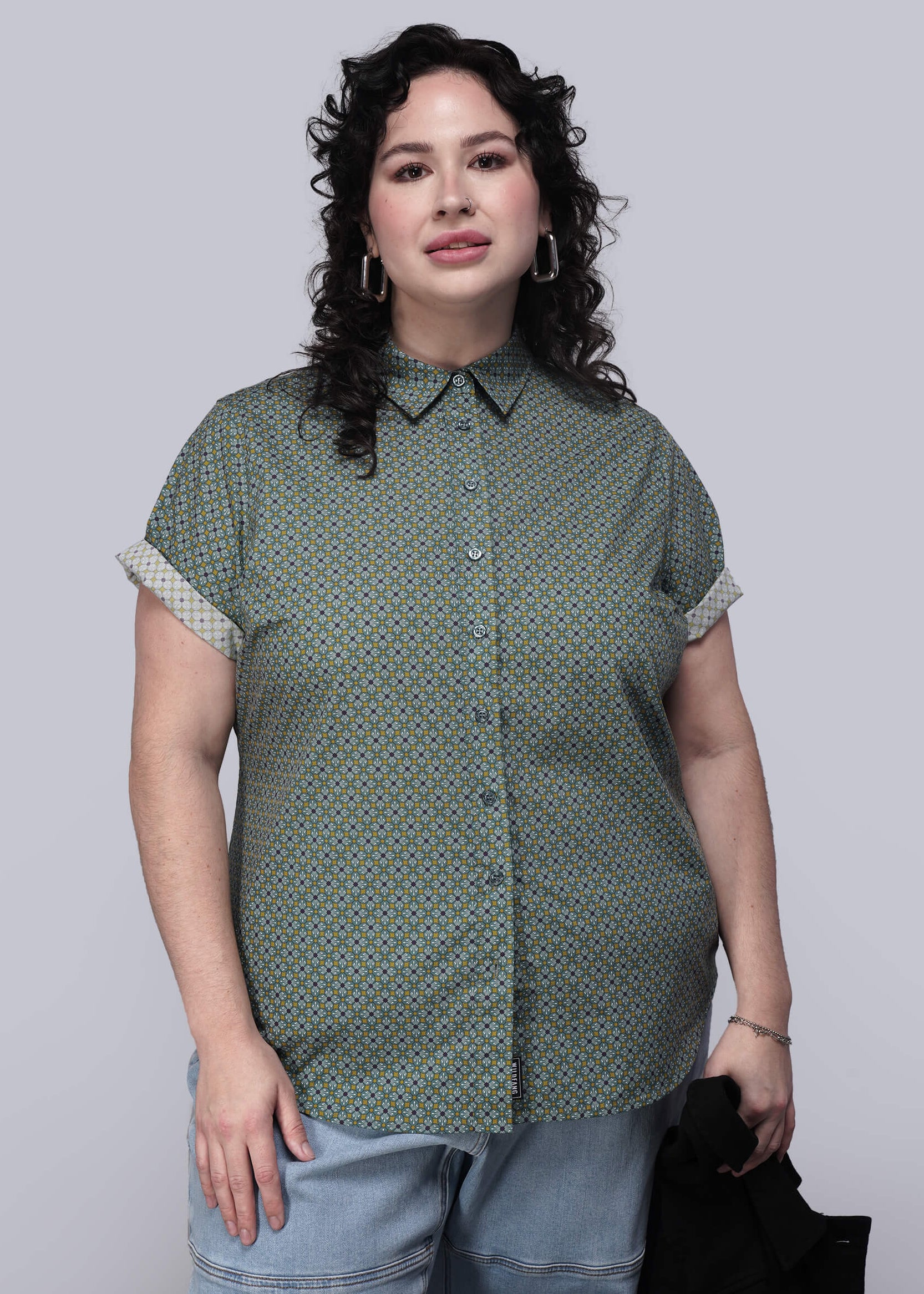 1X=Person wearing a green patterned shirt and light blue jeans against a plain background