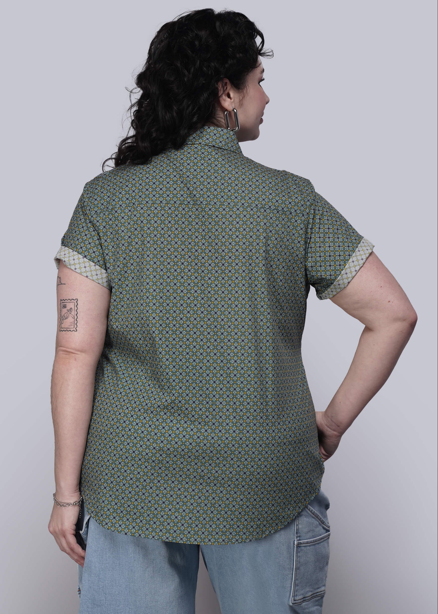 1X=Person wearing a green patterned shirt with short sleeves on a plain background