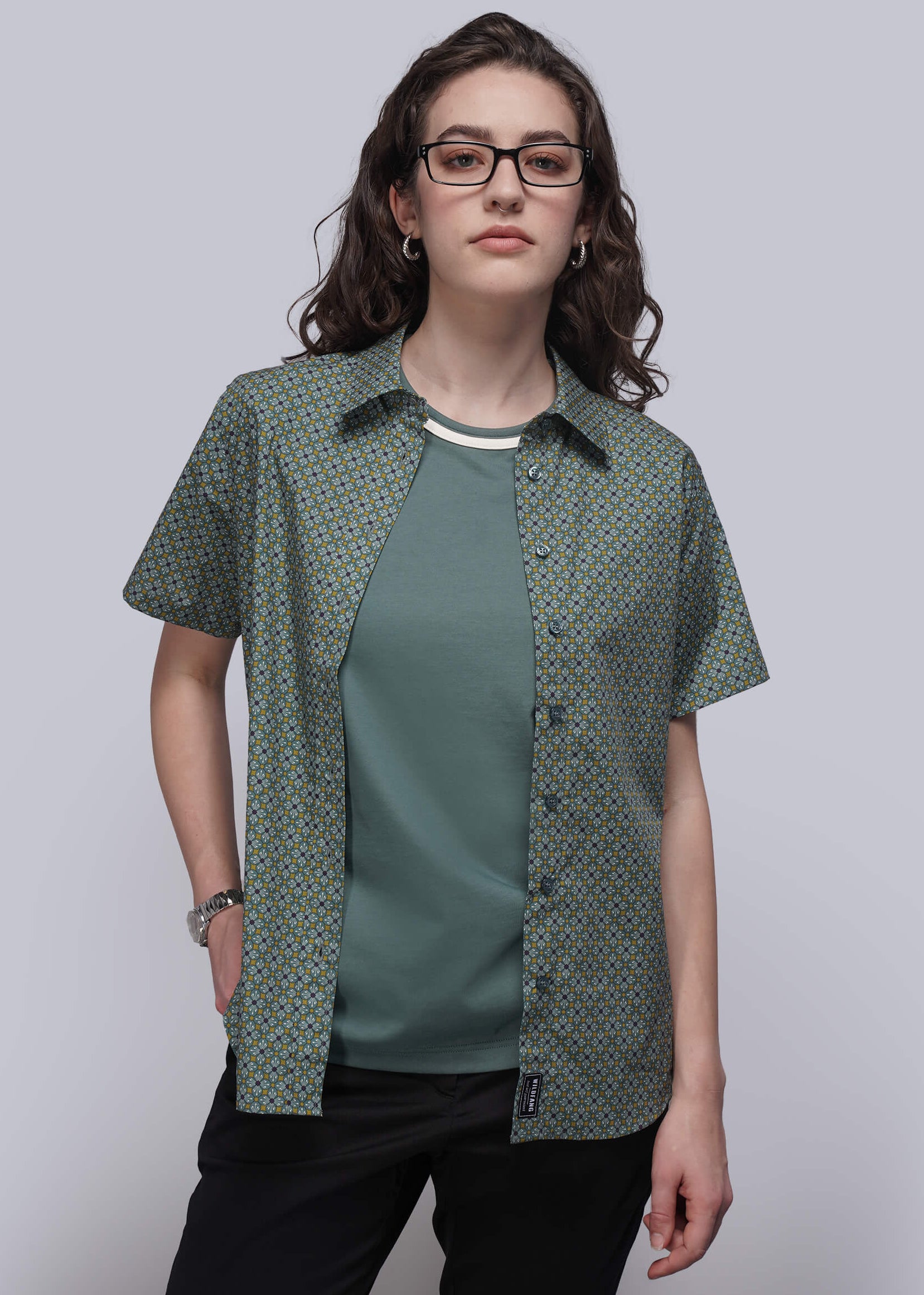S=Person wearing a green patterned shirt over a teal top on a plain background