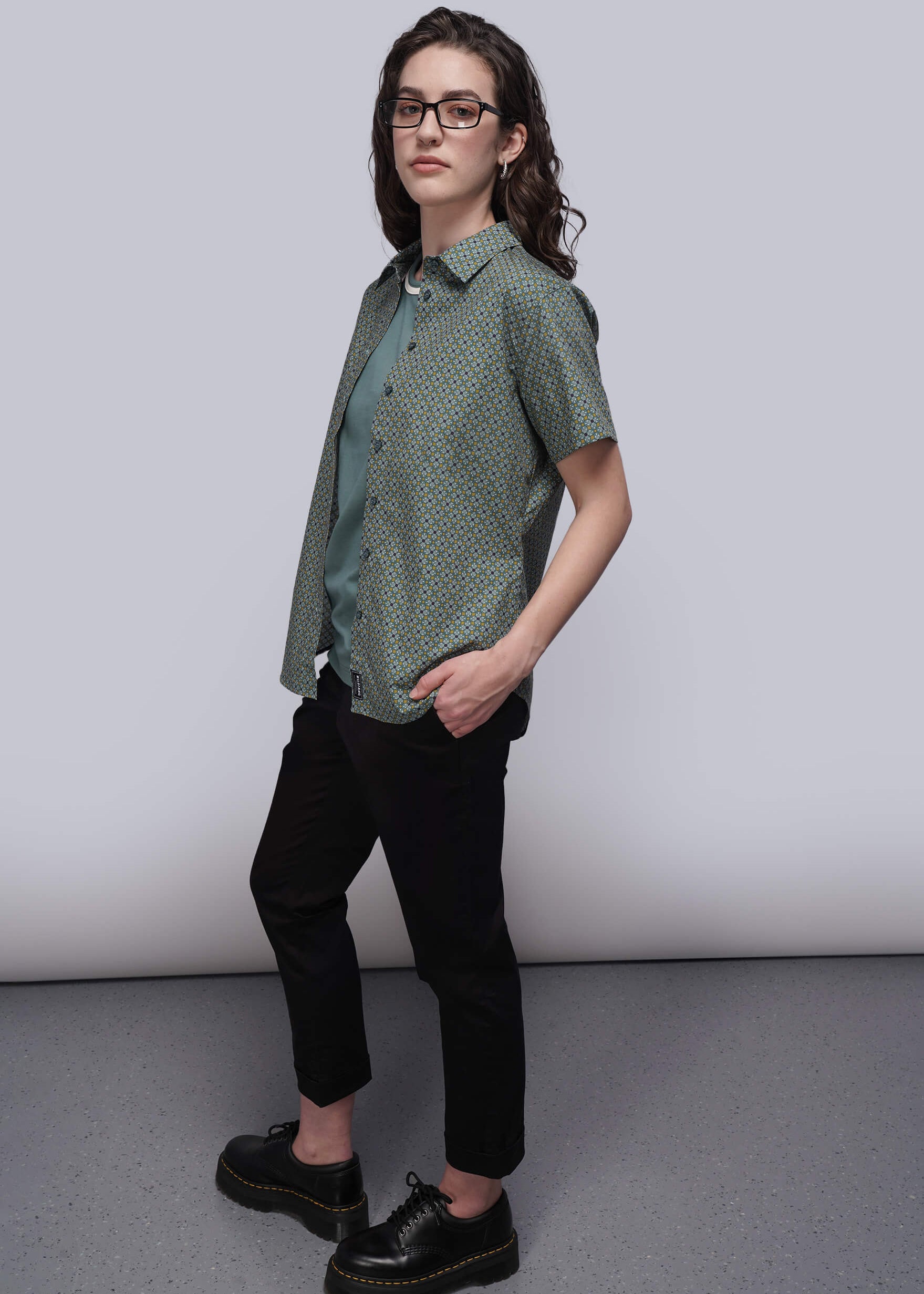 S=Person wearing a green patterned shirt, black pants, and black shoes on a plain background