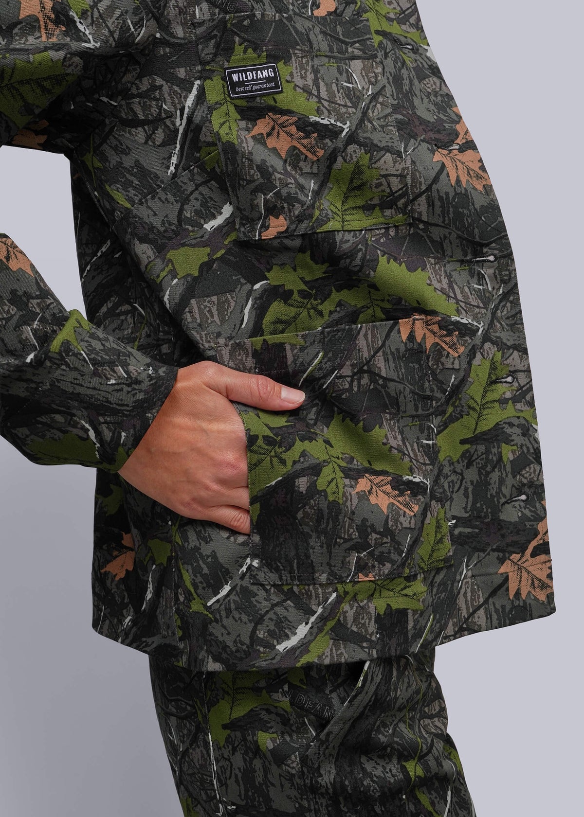 S=Close-up of a person wearing a camouflage jacket with a visible chest pocket and a small black brand patch reading WILDFANG, against a light gray studio background.