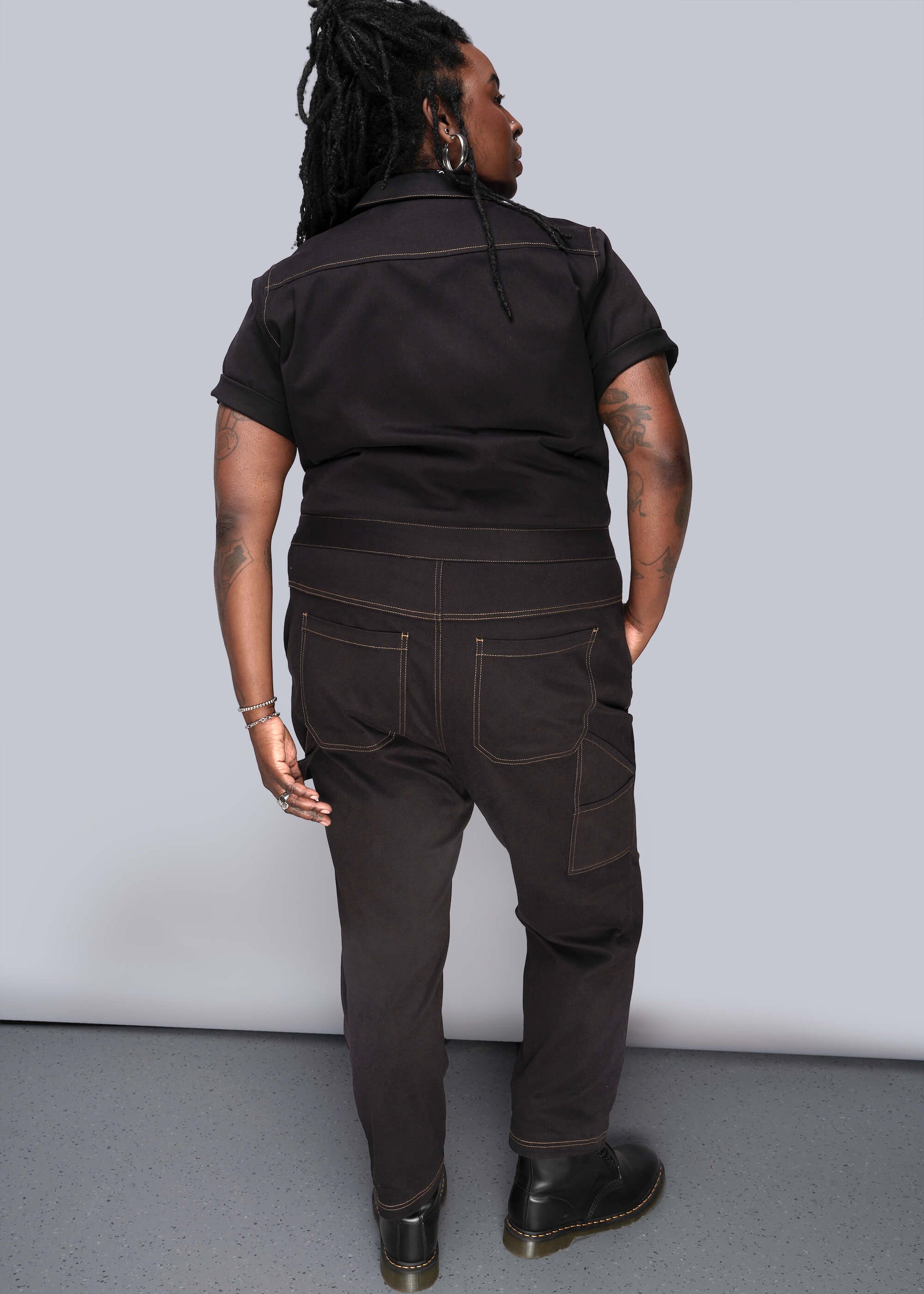 1X=Shown from back, person wears black short sleeved coverall with black boots in front of grey background.