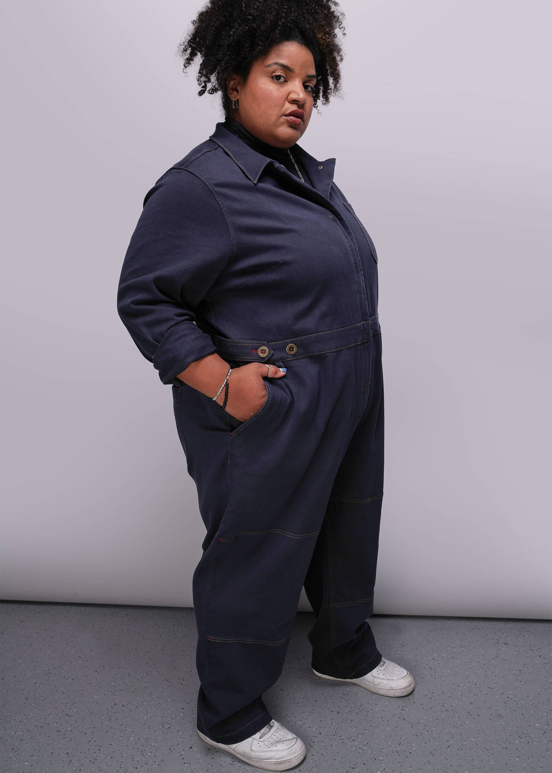 1X=Person wearing a navy blue jumpsuit against a plain background