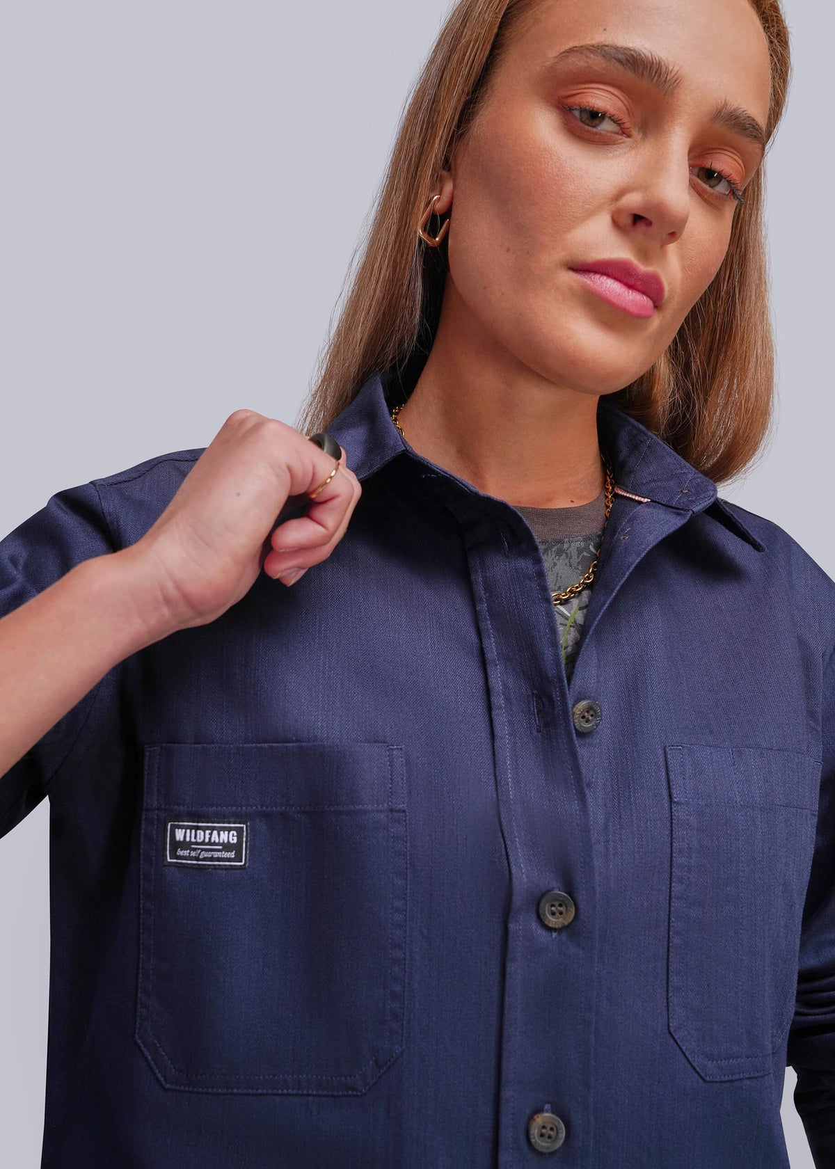 S=A woman modeling a navy blue long-sleeve button-up shirt with a chest pocket, against a solid light gray background.