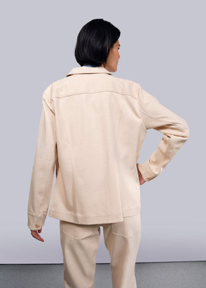 S=A person with short dark hair stands back to the camera wearing The Essential Denim Utility Jacket and matching pants in light beige. The outfit offers stretch comfort for all-day wear, highlighted against a plain light gray background, enhancing the sleek design of the ensemble.