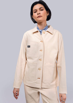 S=A person with short dark hair wears The Essential Denim Utility Jacket, known for its deep pockets and stretch comfort, over a light blue shirt. They stand against a plain white background, looking slightly to the side with a neutral expression.