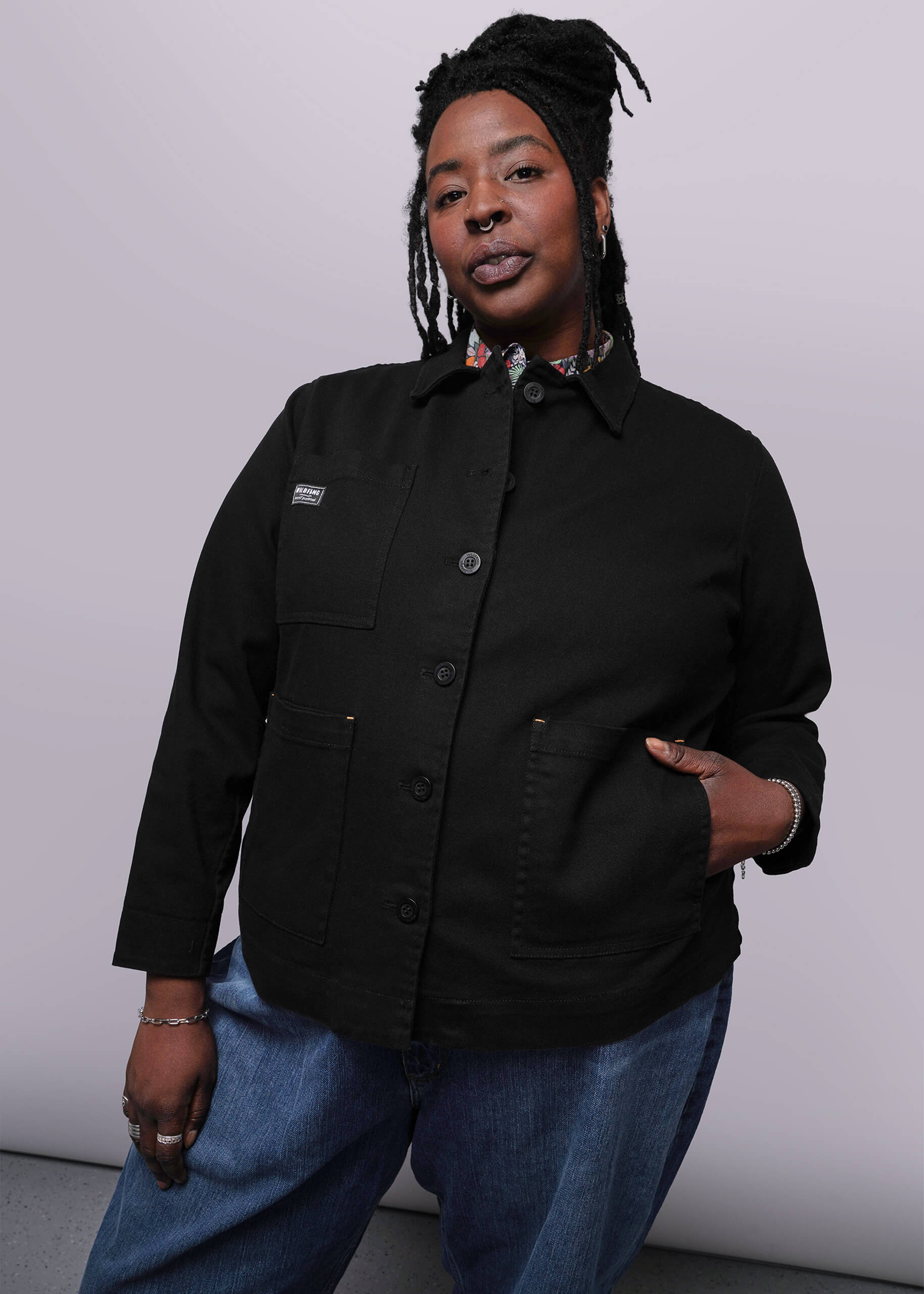 1X=Person wearing a black jacket and blue jeans against a white background