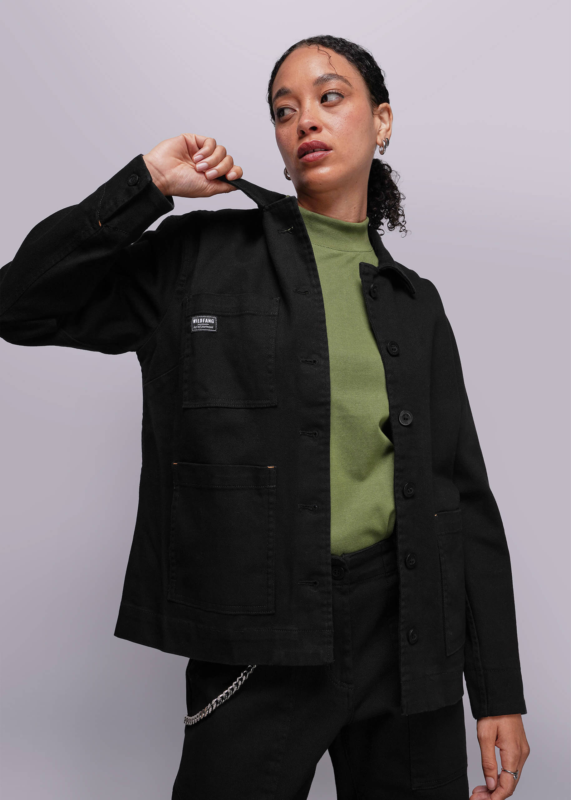 Person wearing a black denim jacket with a visible brand logo on a plain background