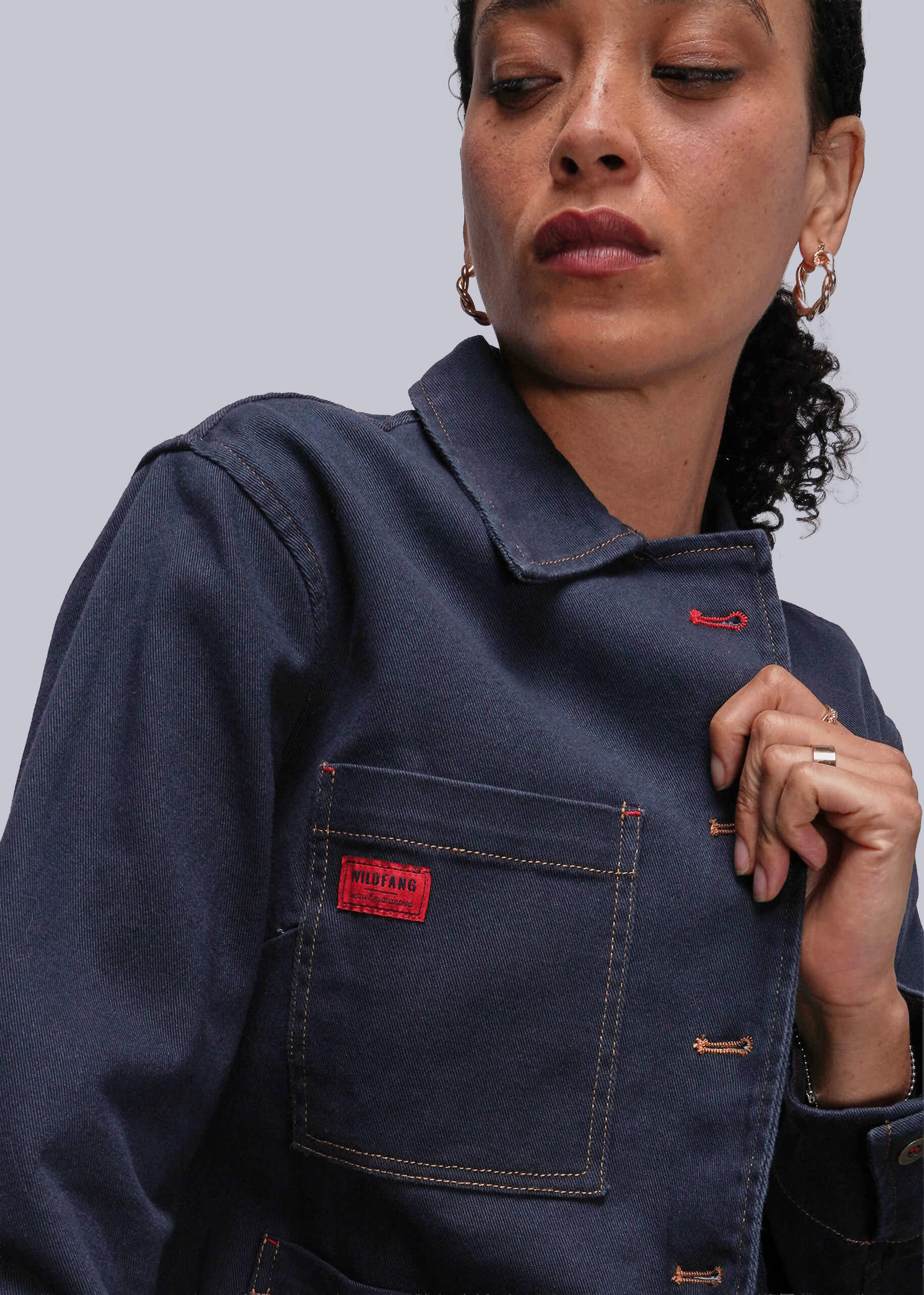 Person wearing a navy blue jean jacket with a red patch on a gray background