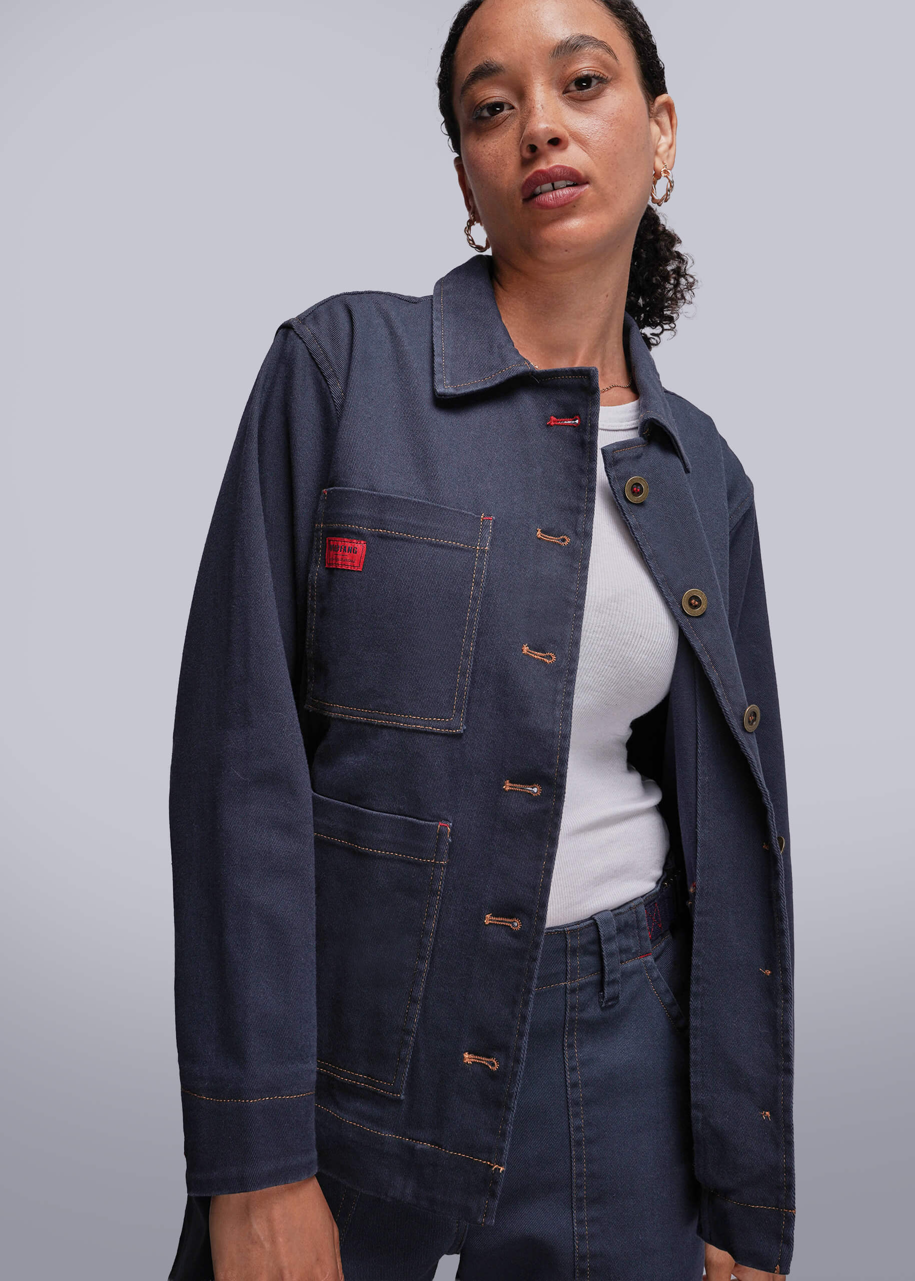 Person wearing a dark blue jean jacket with a red label on a light gray background