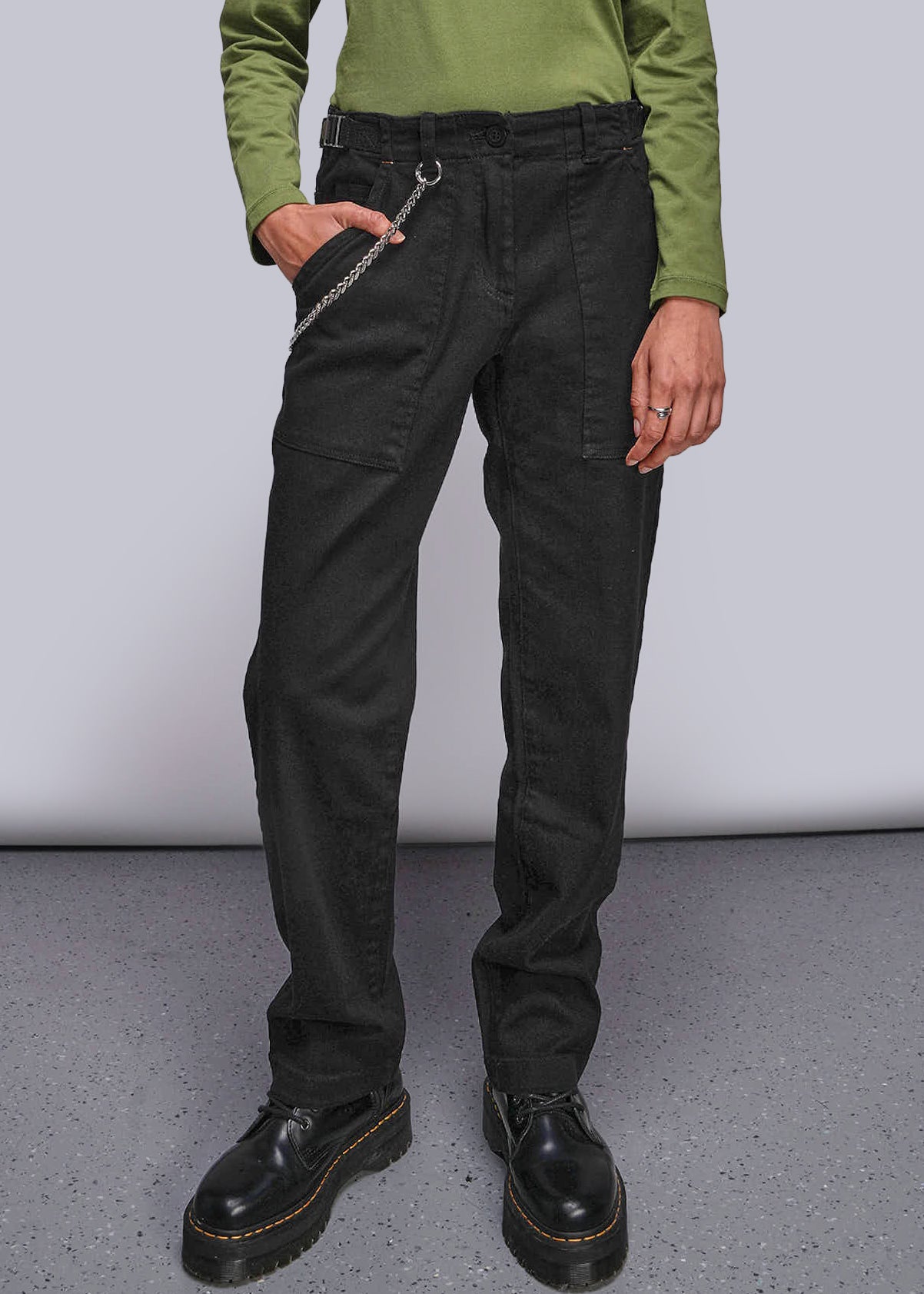 Person wearing black pants and green shirt against a plain background