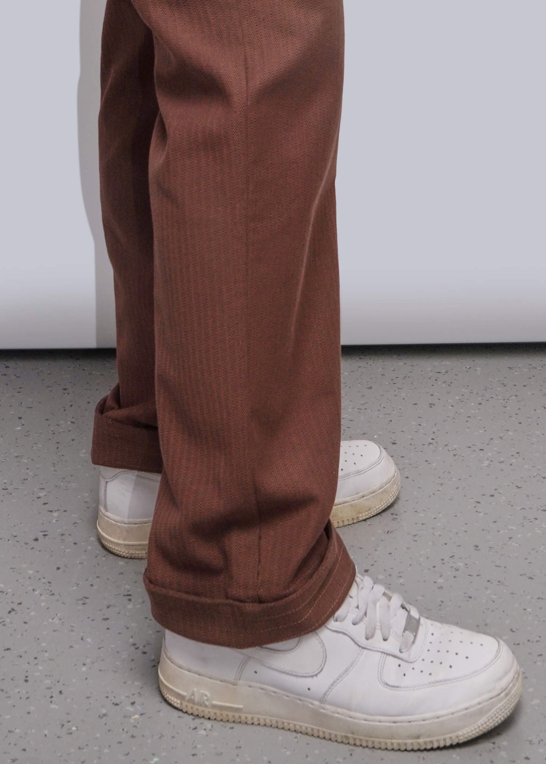 S=Close up of brown coverall pant cuffs on model wearing white sneakers, set against grey background.