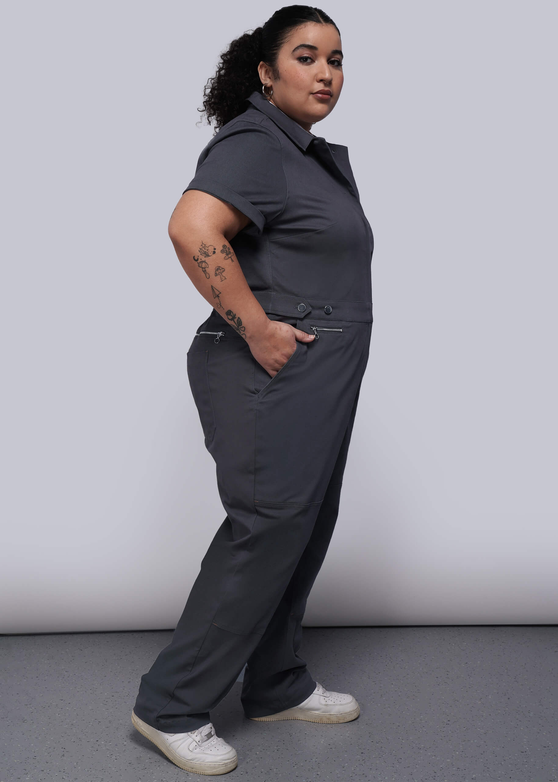 1X=Person wearing a dark grey jumpsuit and sneakers with a plain background