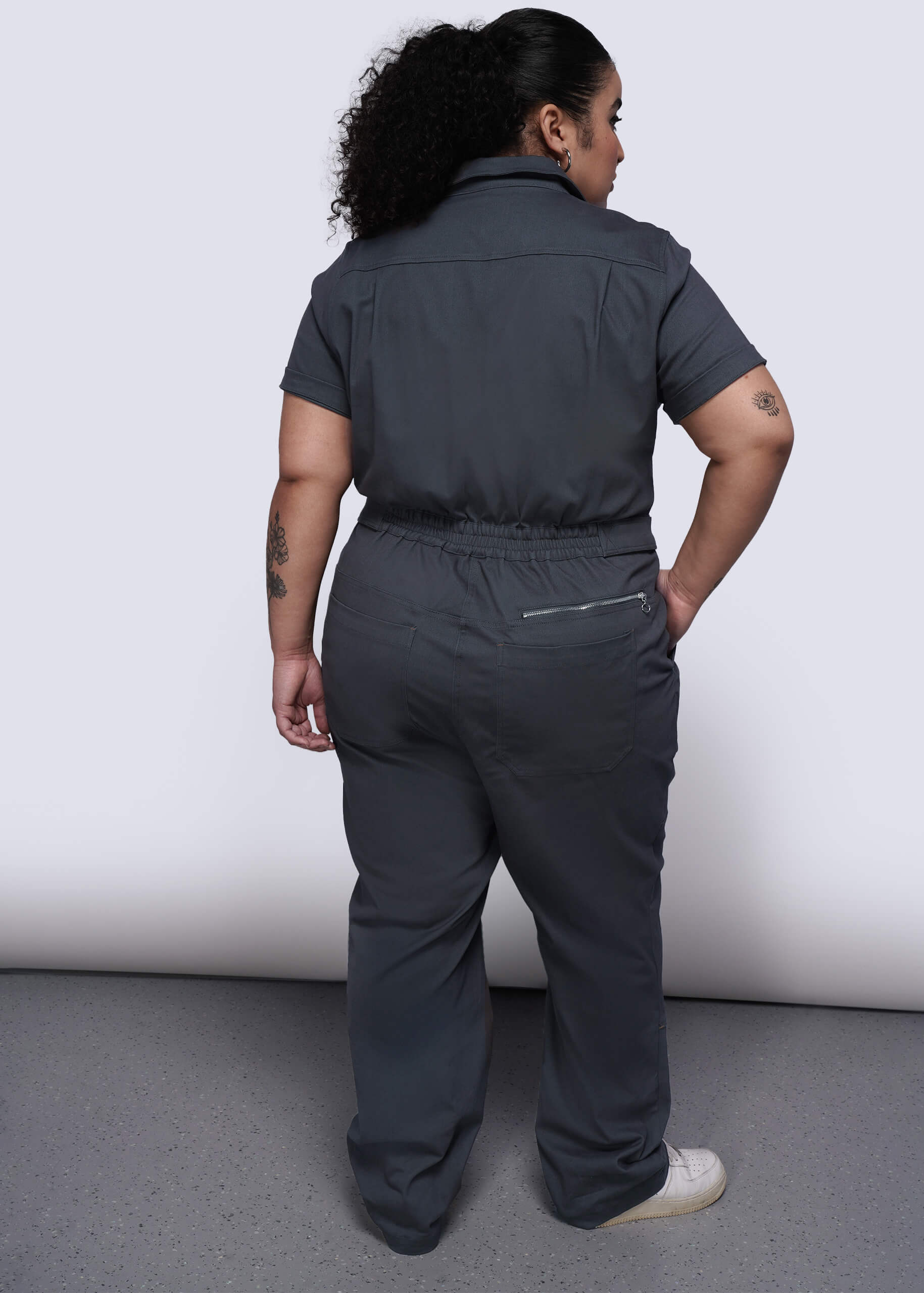 1X=Back of person wearing a black jumpsuit against a white background