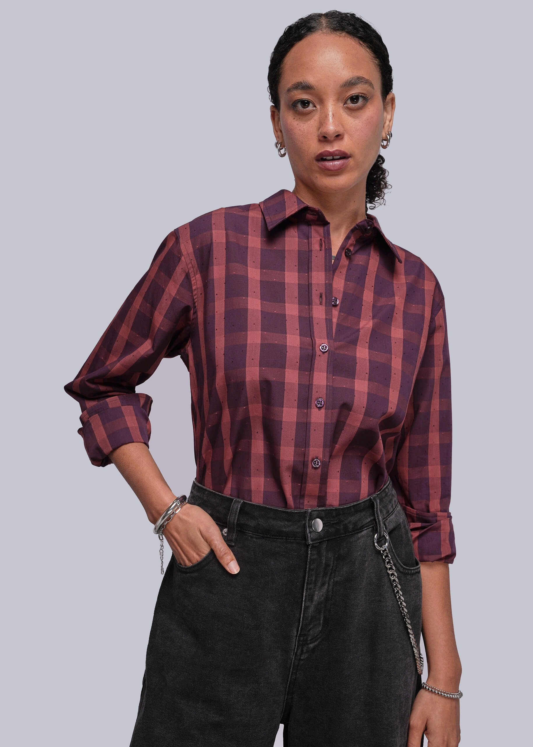 Person wearing a red and burgundy plaid shirt with rolled-up sleeves against a plain background