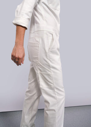 S=A person in The Essential Long Sleeve Herringbone Coverall, made from white herringbone cotton and featuring a full-length zipper and 10 pockets, stands against a light gray background. They are shown from the shoulder down with their arm slightly bent.