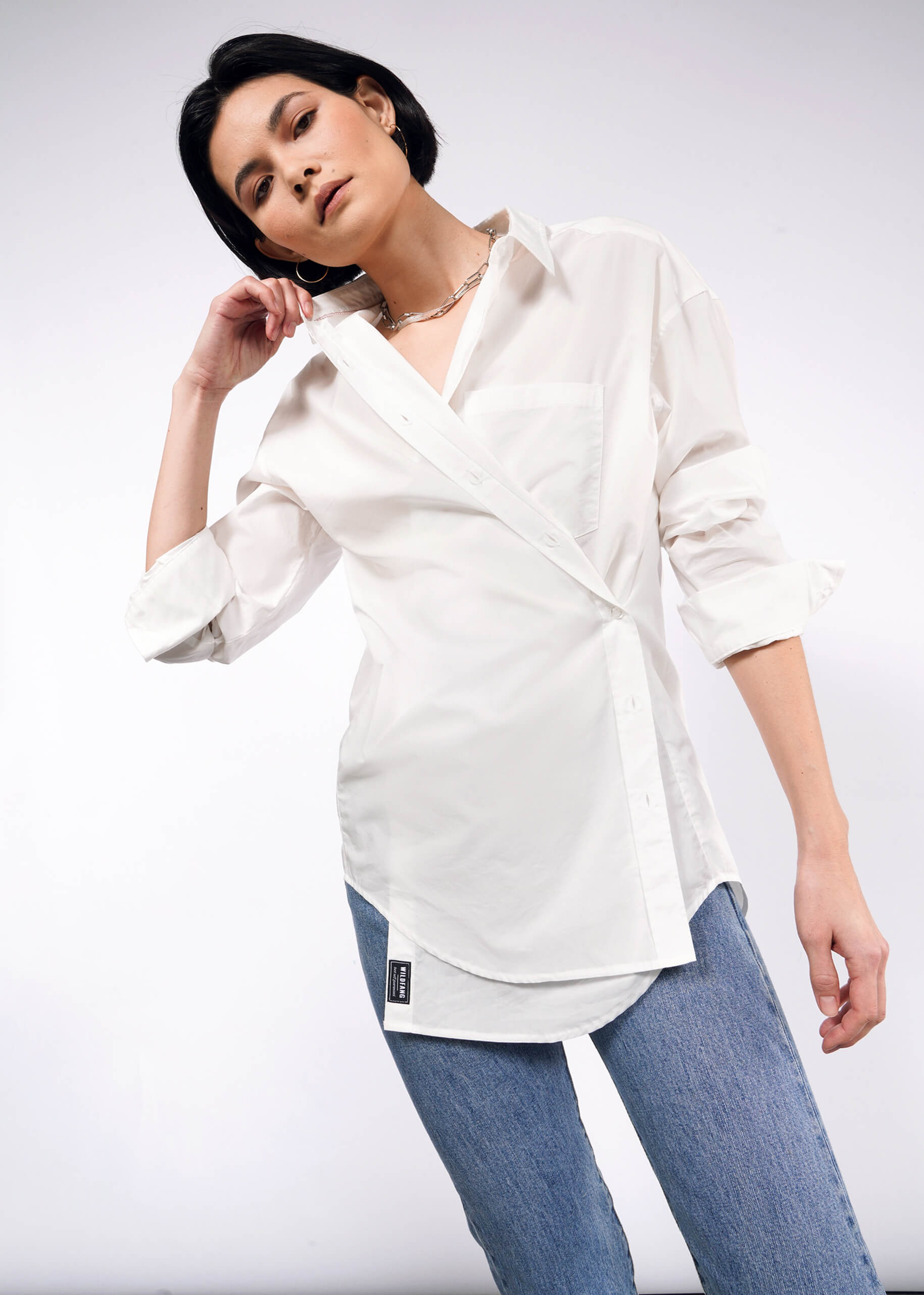 S=Front view of model with short black hair wearing The Essential Long Sleeve Oversized Button Up in white with jeans.