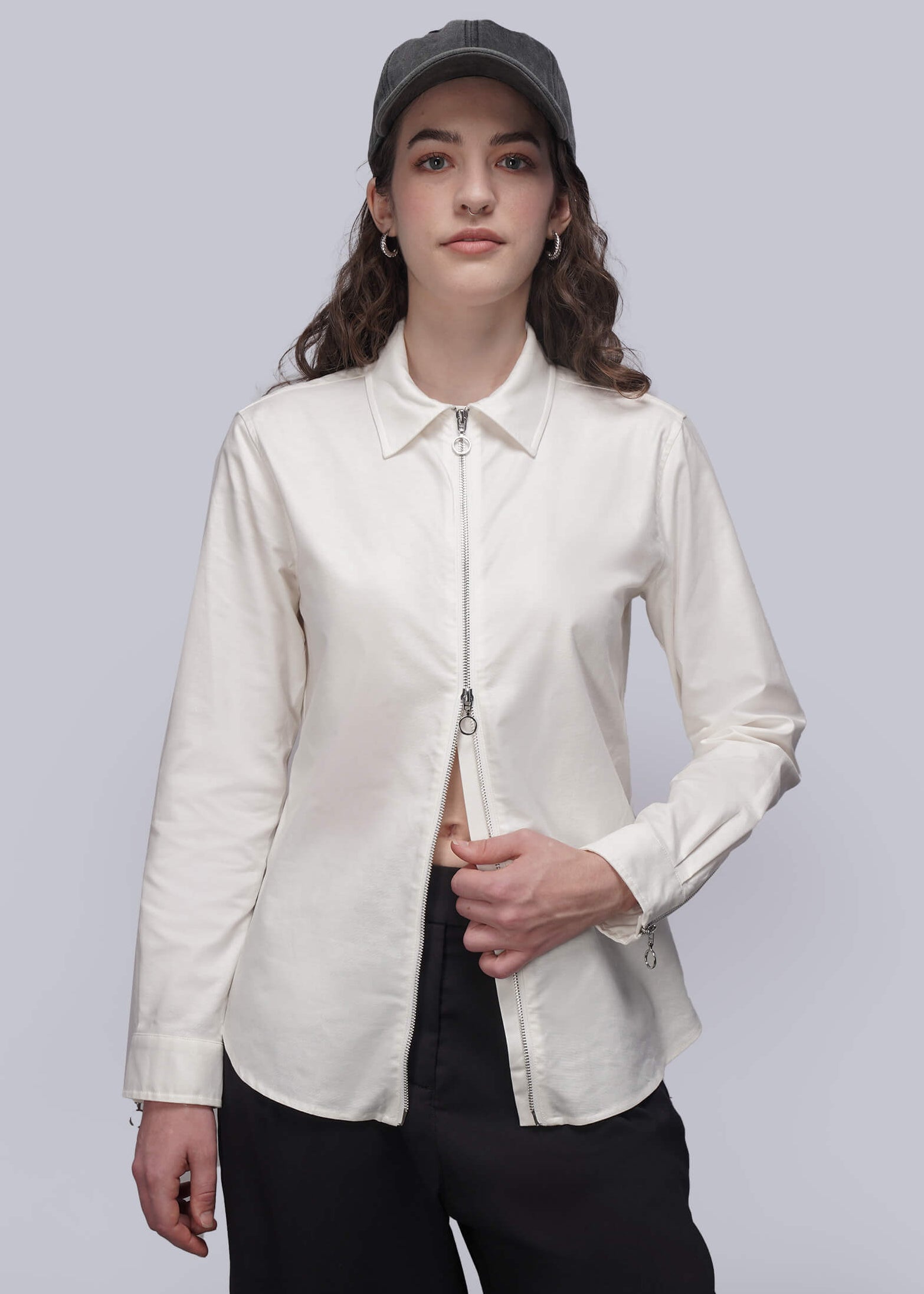 Person wearing a white shirt with a zipper and black pants on a plain background