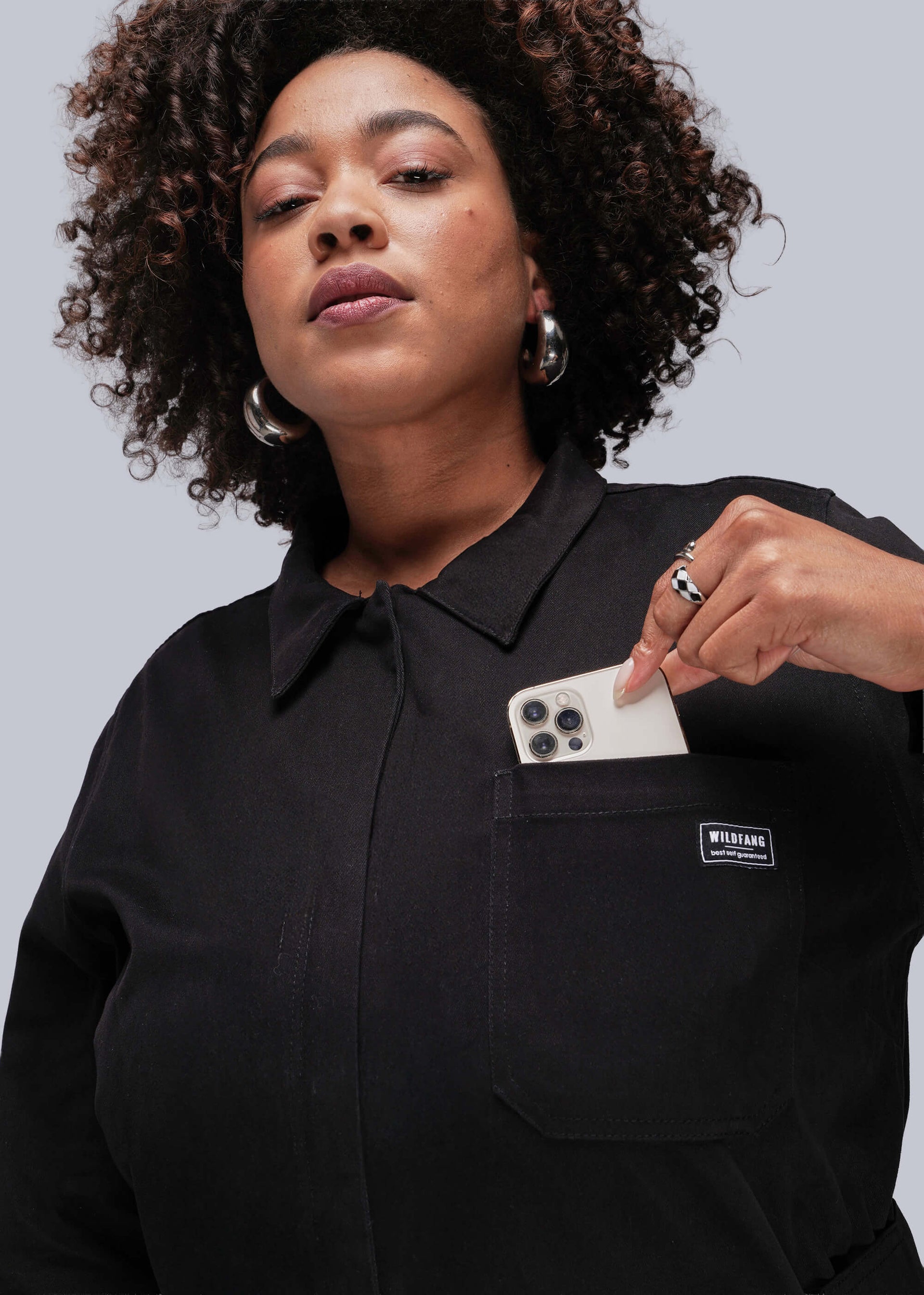 1X=Person wearing a black shirt with a visible brand logo, holding a smartphone.