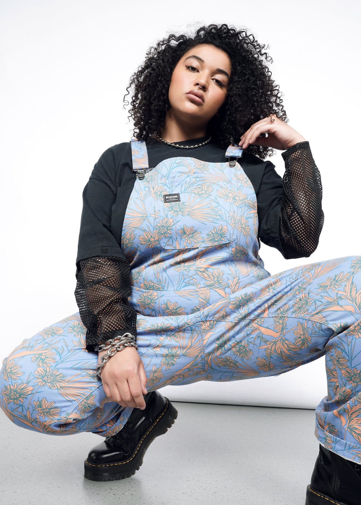 Model wearing the Essential Overall in Flower Press Periwinkle in size 1X, wearing black mesh long sleeve shirt and black platform shoes.