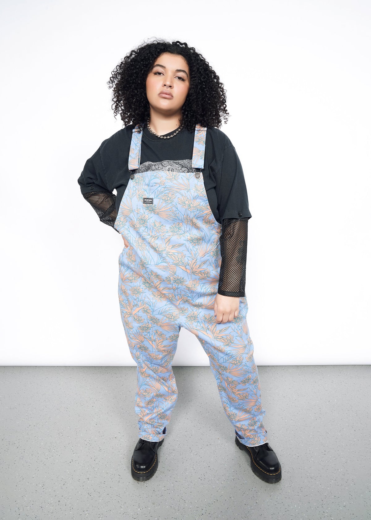 Model wearing the Essential Overall in Flower Press Periwinkle in size 1X, wearing black mesh long sleeve shirt and black platform shoes.
